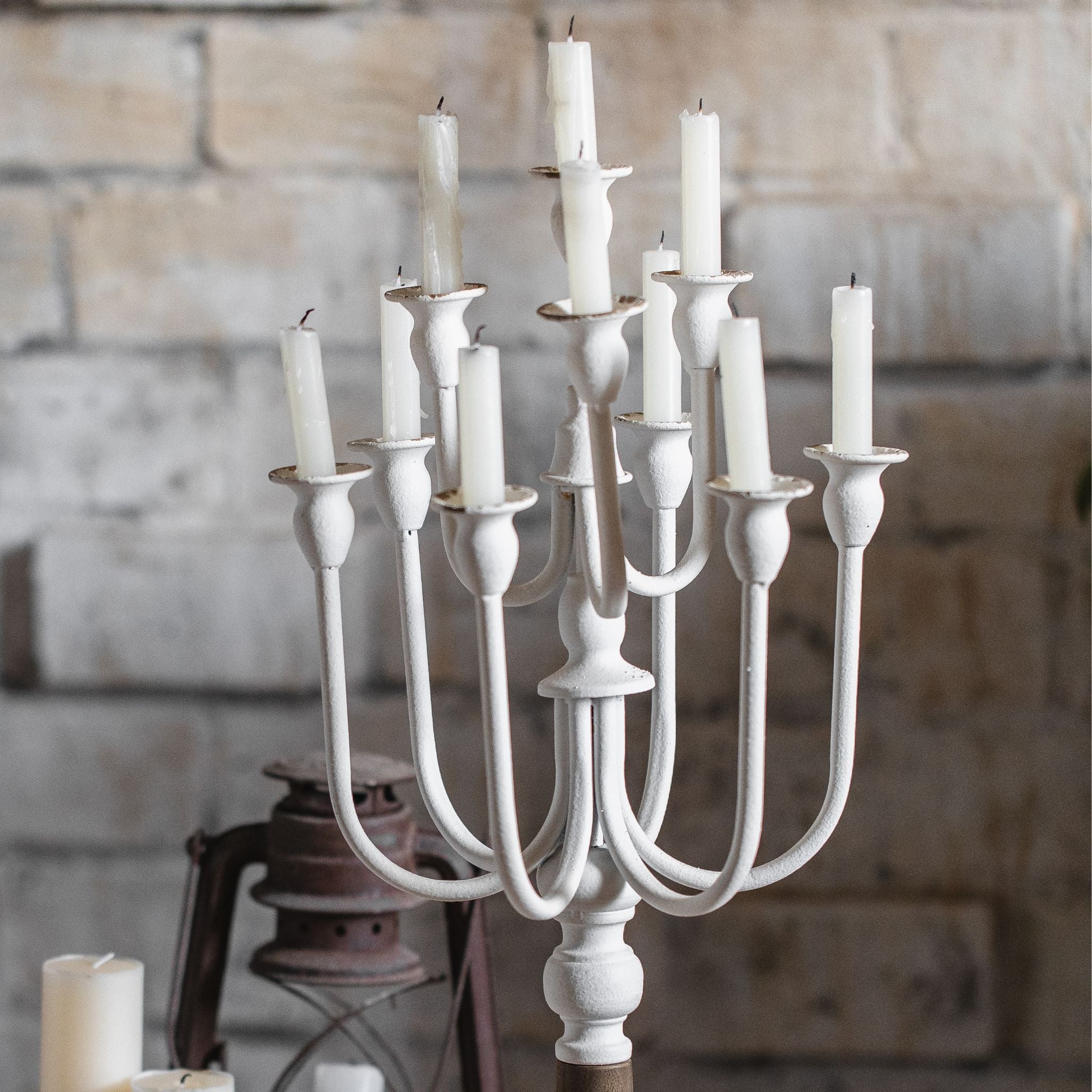 Close-up detail of Étienne candelabra's twelve curved iron arms each holding a tapered white candle, showing the distressed whitewash finish and tulip-shaped cups