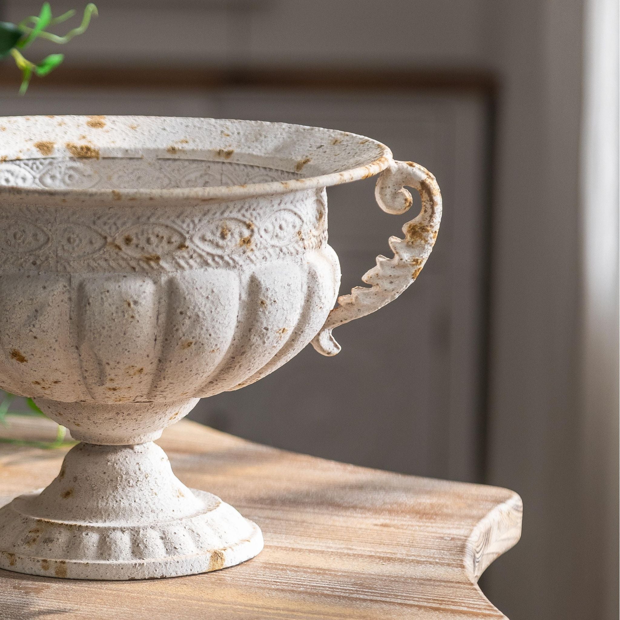 Angled view of the Fabien urn scroll handle and pedestal foot in chalky antique-white metal.
