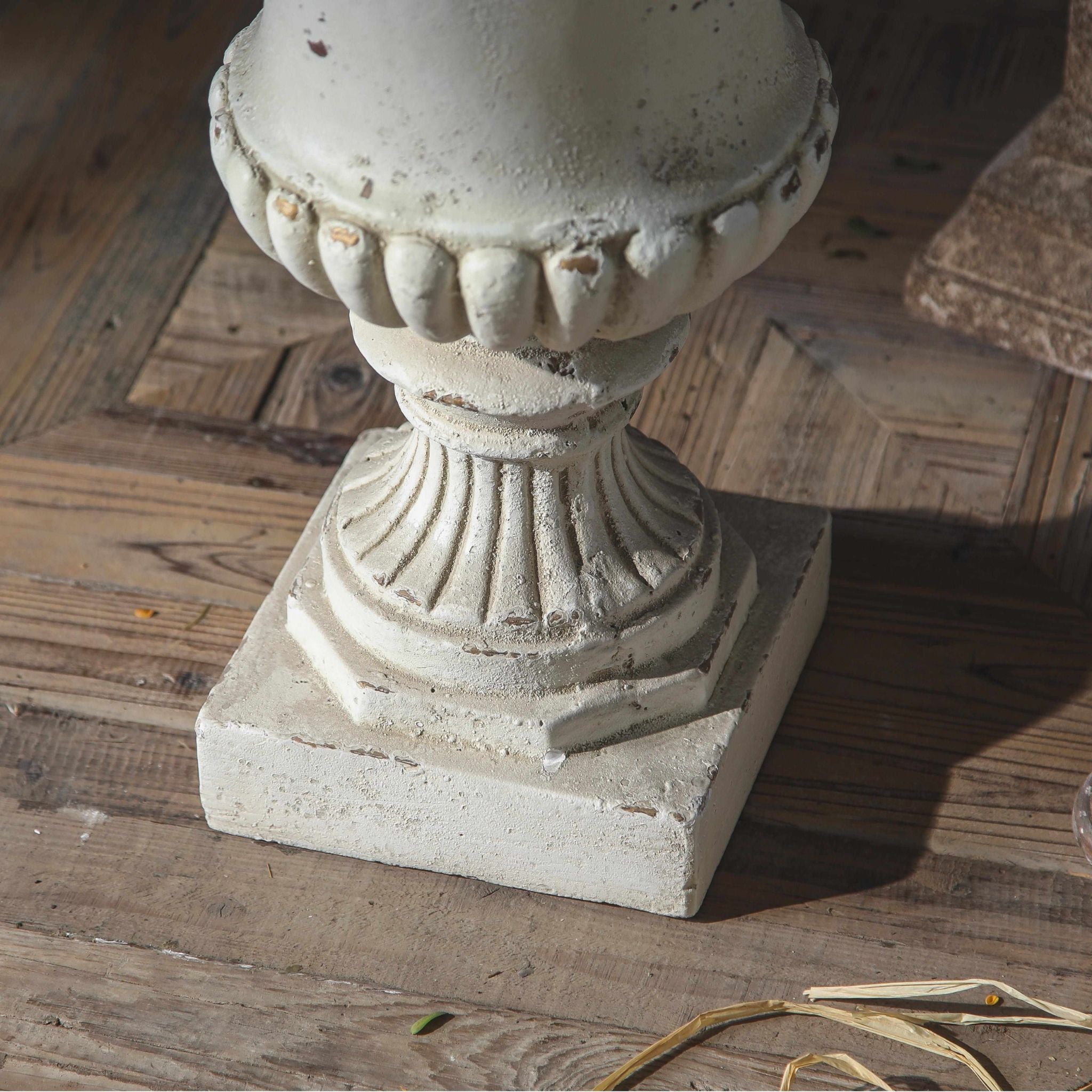 Close-up of the Florentine urn fluted stem and stepped plinth, chipped antique white finish over a warm undertone.