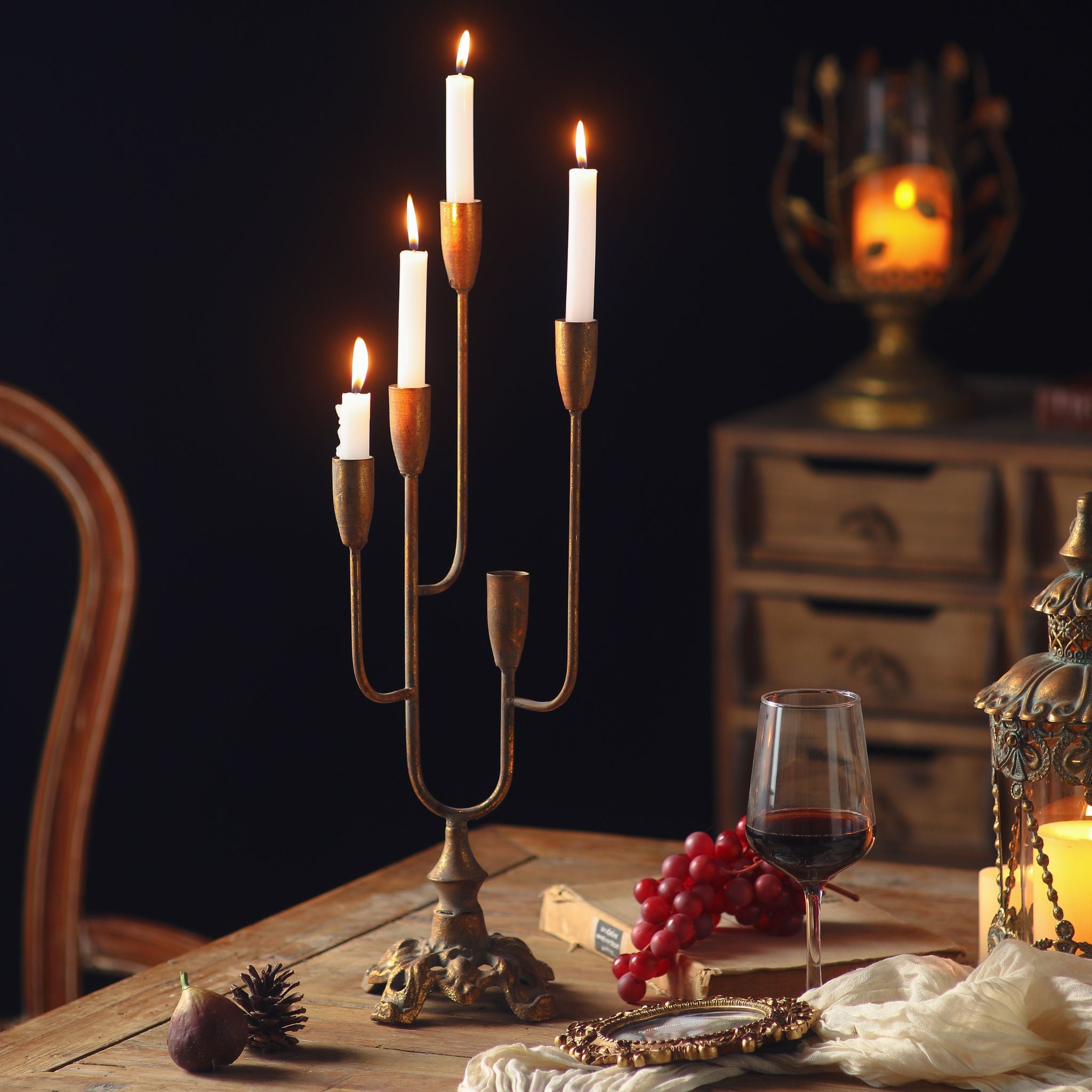 Lisette French Provincial five-light candelabra in antique gold, holding lit white taper candles on graduated arms, on a timber table with wine and grapes.