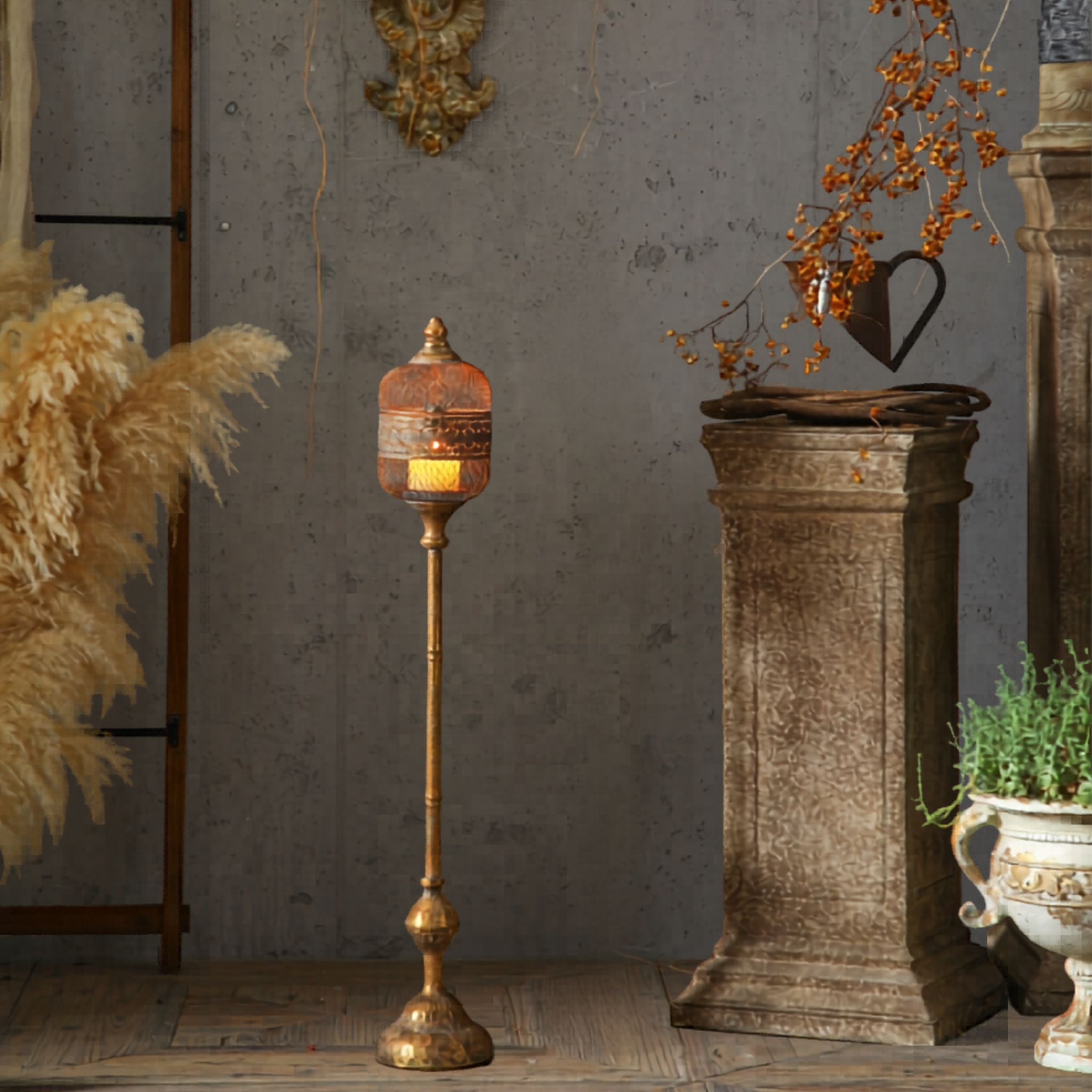Astrid French Provincial standing candle lantern in antique gold aged metal, pierced diamond mesh head on a turned pedestal, lit candle inside, styled beside pampas grass.