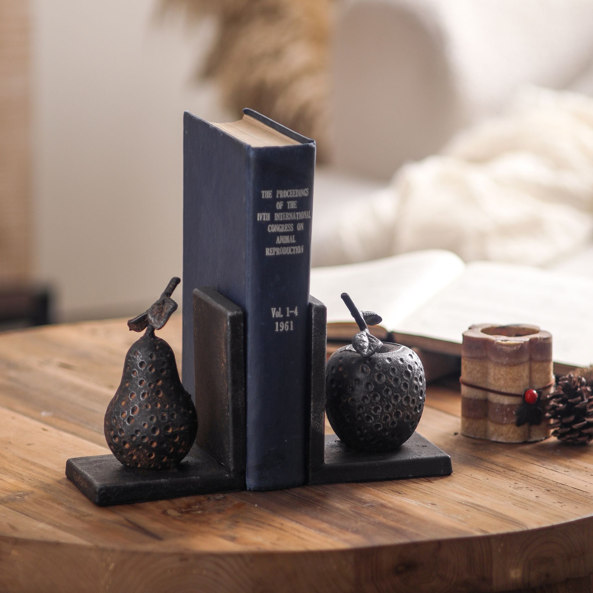Poire cast iron pear and apple bookends holding a vintage navy book upright on a round wooden table.