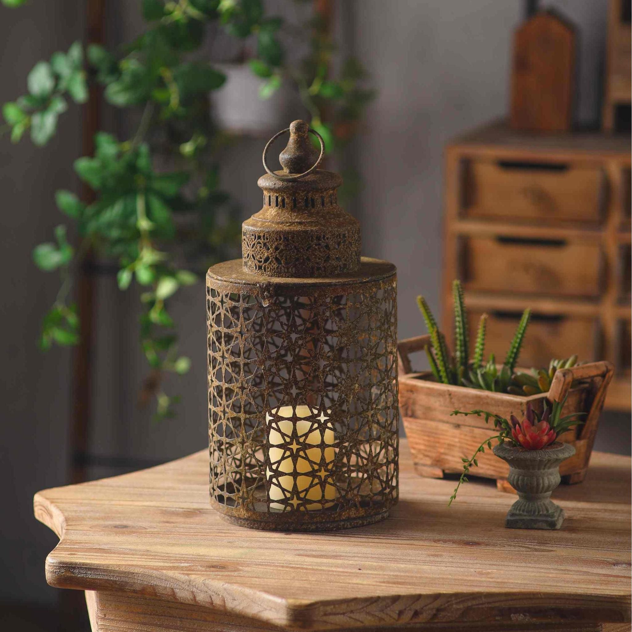 Yannick French Provincial Moroccan star-pierced lantern in weathered rust aged metal, lit candle inside, on a timber table with succulents and greenery.
