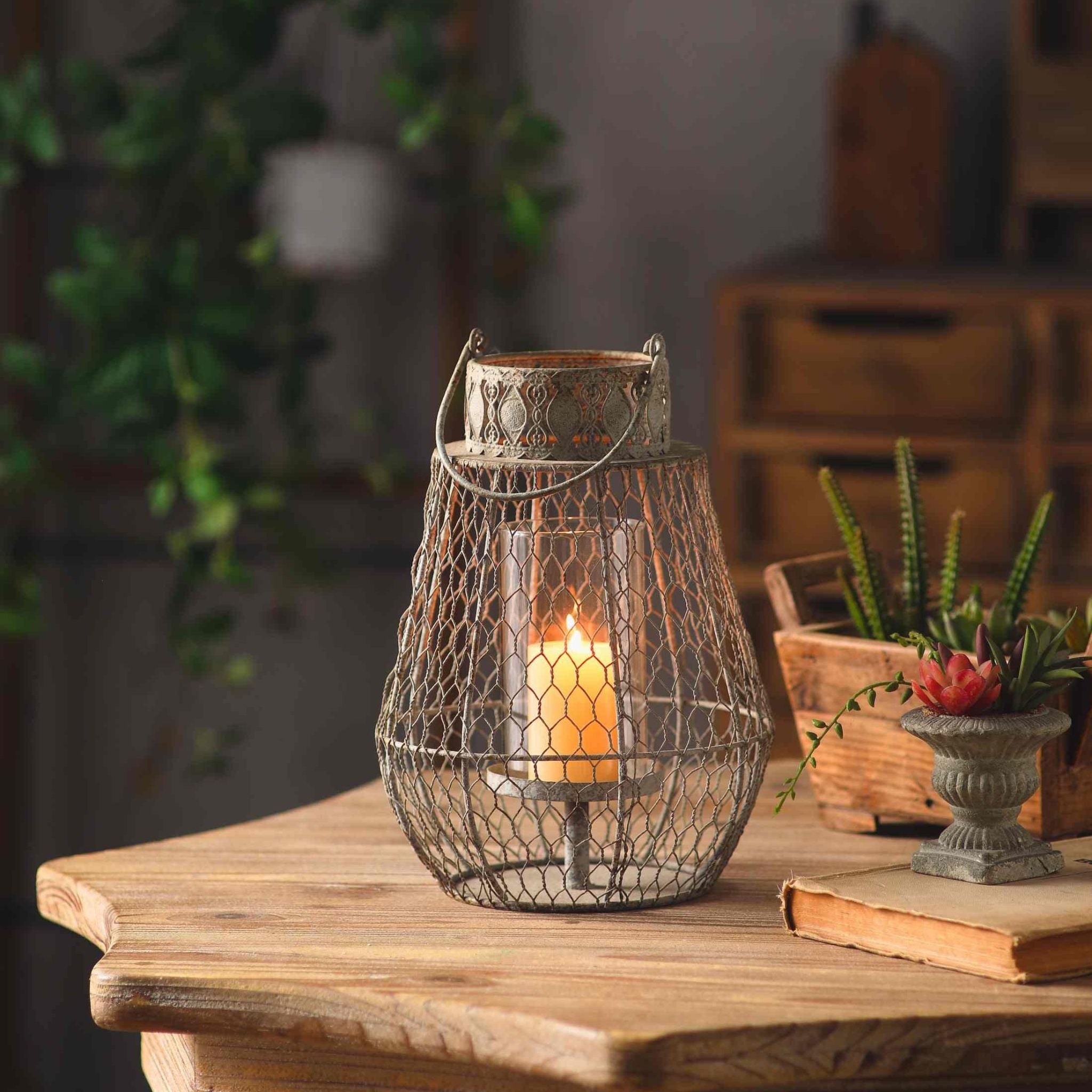 Martine French Provincial wire cage candle lantern in weathered grey, glass insert and lit pillar candle, on a timber table with succulents and an old book.