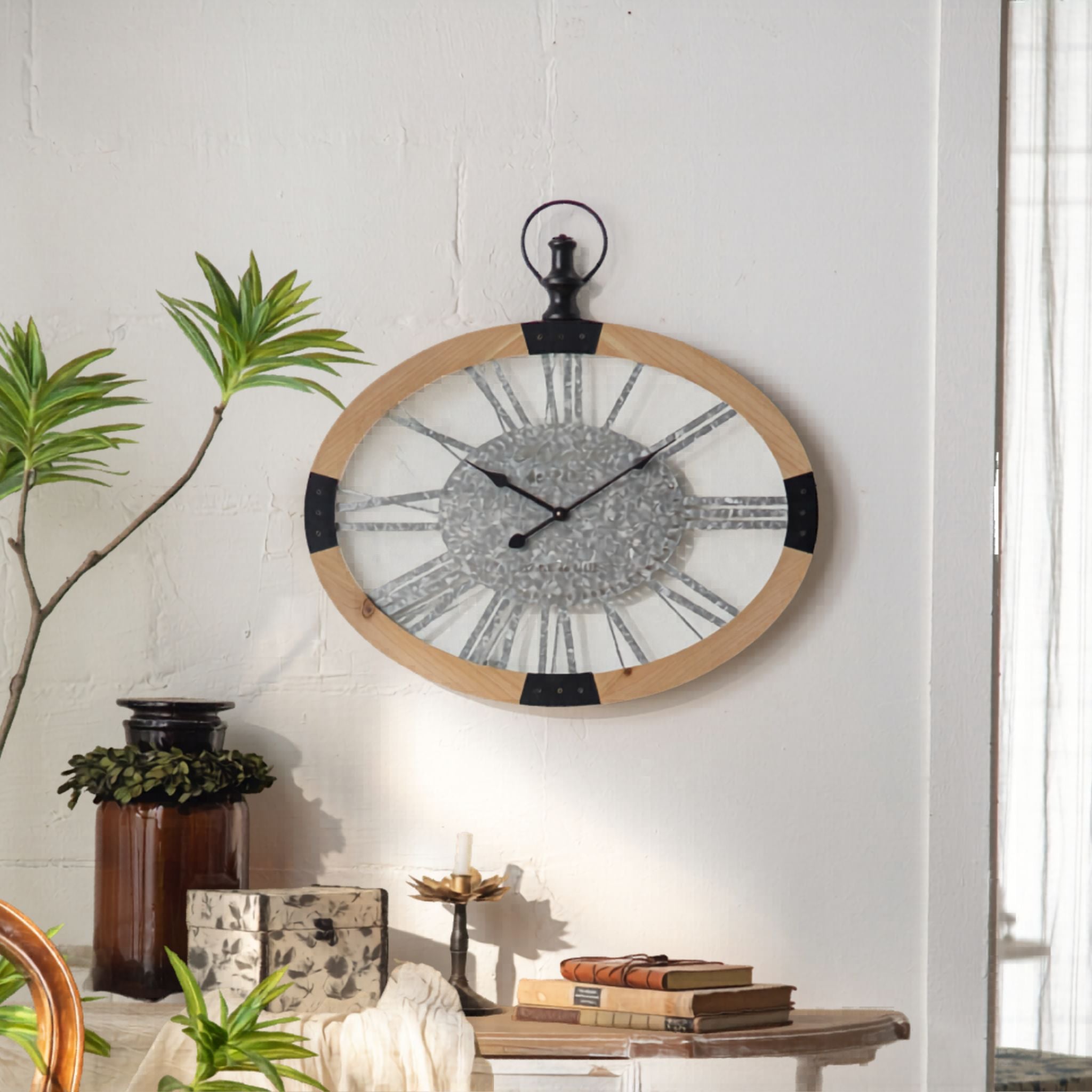 Maude oval wall clock styled on a living room wall above books and a candle