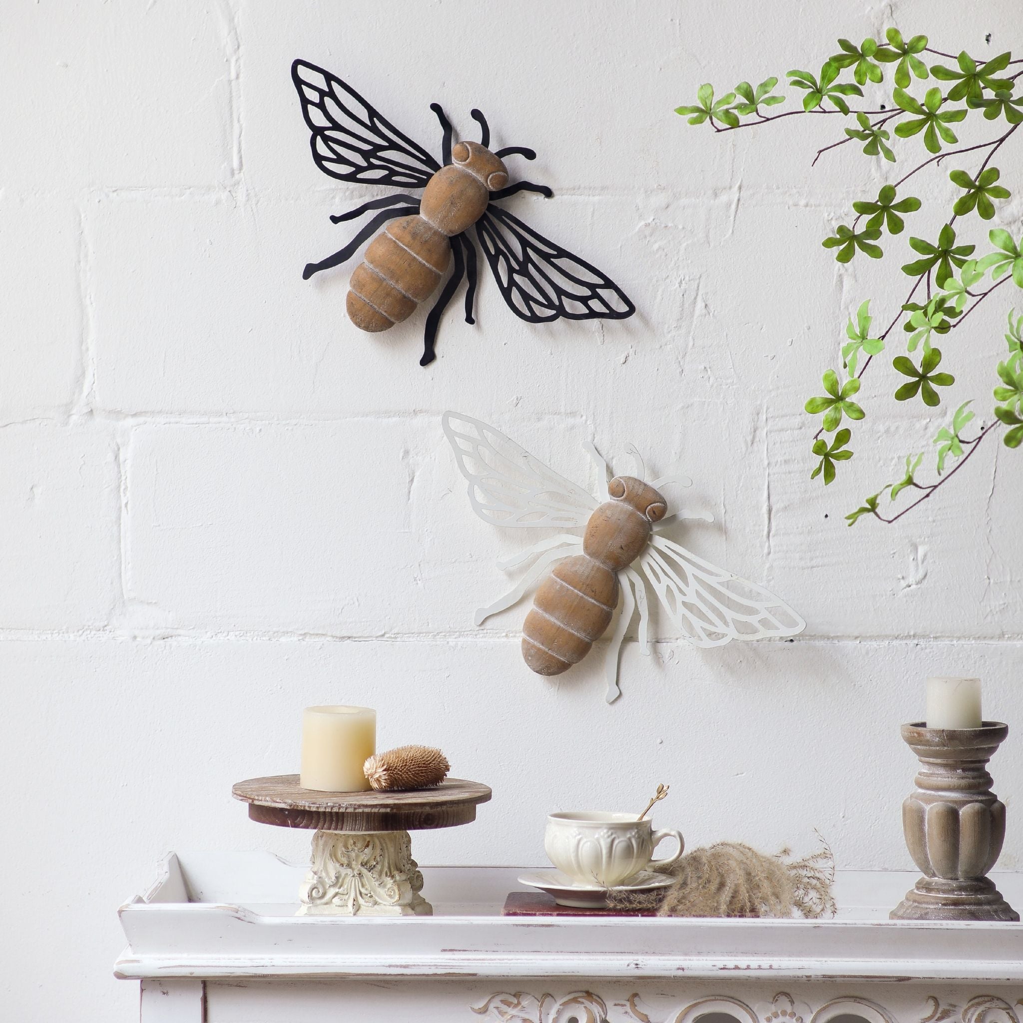 Honey antique white bee styled in a full room context above a console with the Barry black bee, cream candles, pampas grass, and antique pillar holders