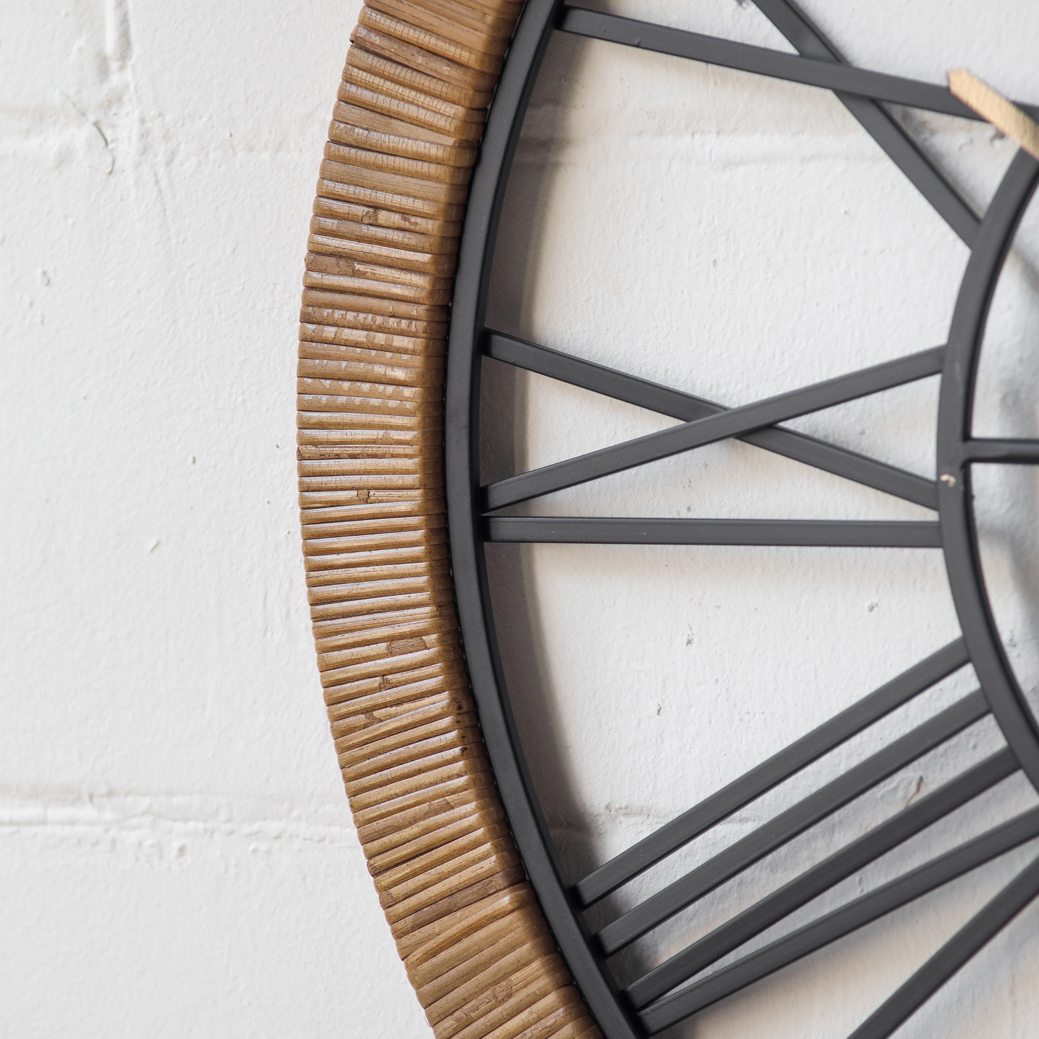 Close-up side detail of Hugo wall clock showing the wrapped rattan texture along the outer frame and black iron Roman numerals