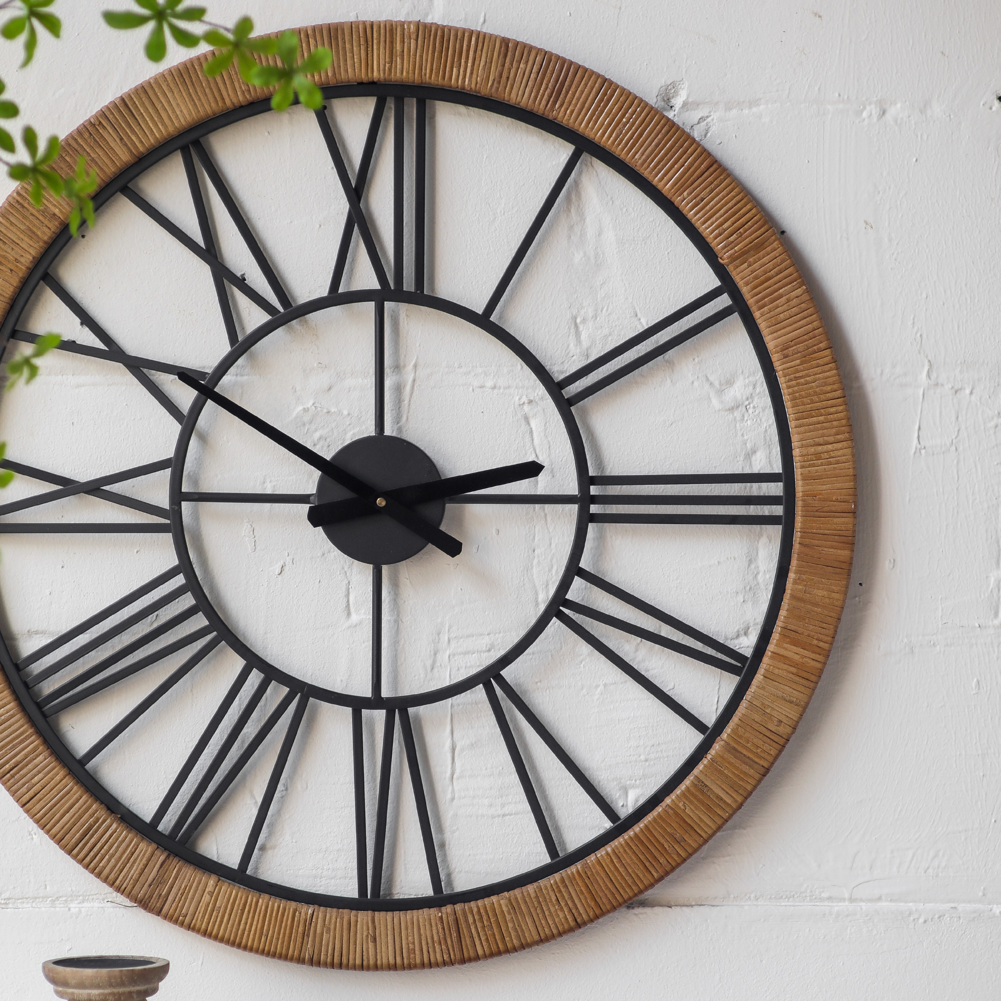 Three-quarter view of Hugo wall clock showing the full rattan-wrapped frame and Roman numeral arrangement