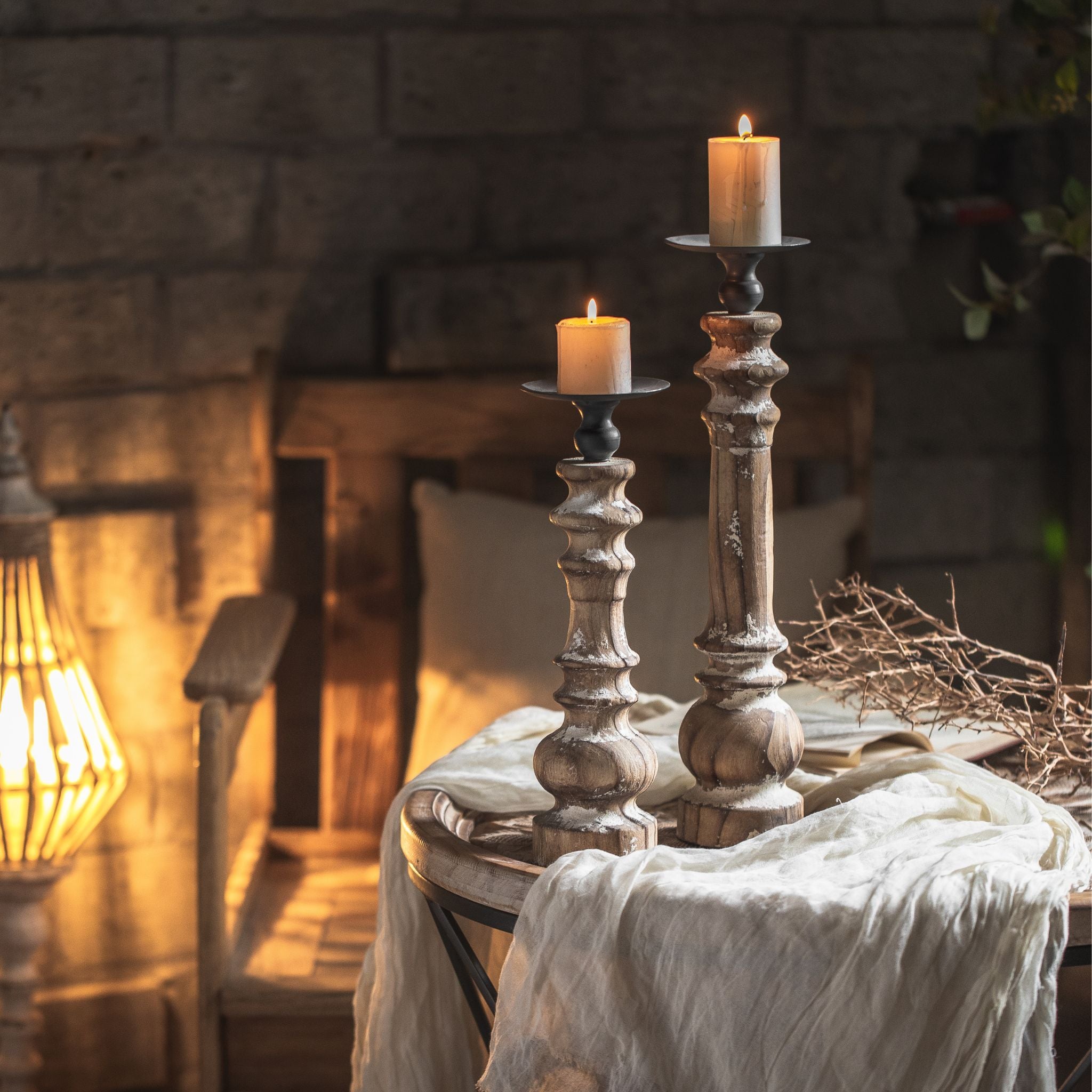 Jacques French Provincial pillar candle holder in distressed white turned timber with an aged metal dish, lit pillar candle, shown taller alongside the shorter size. 