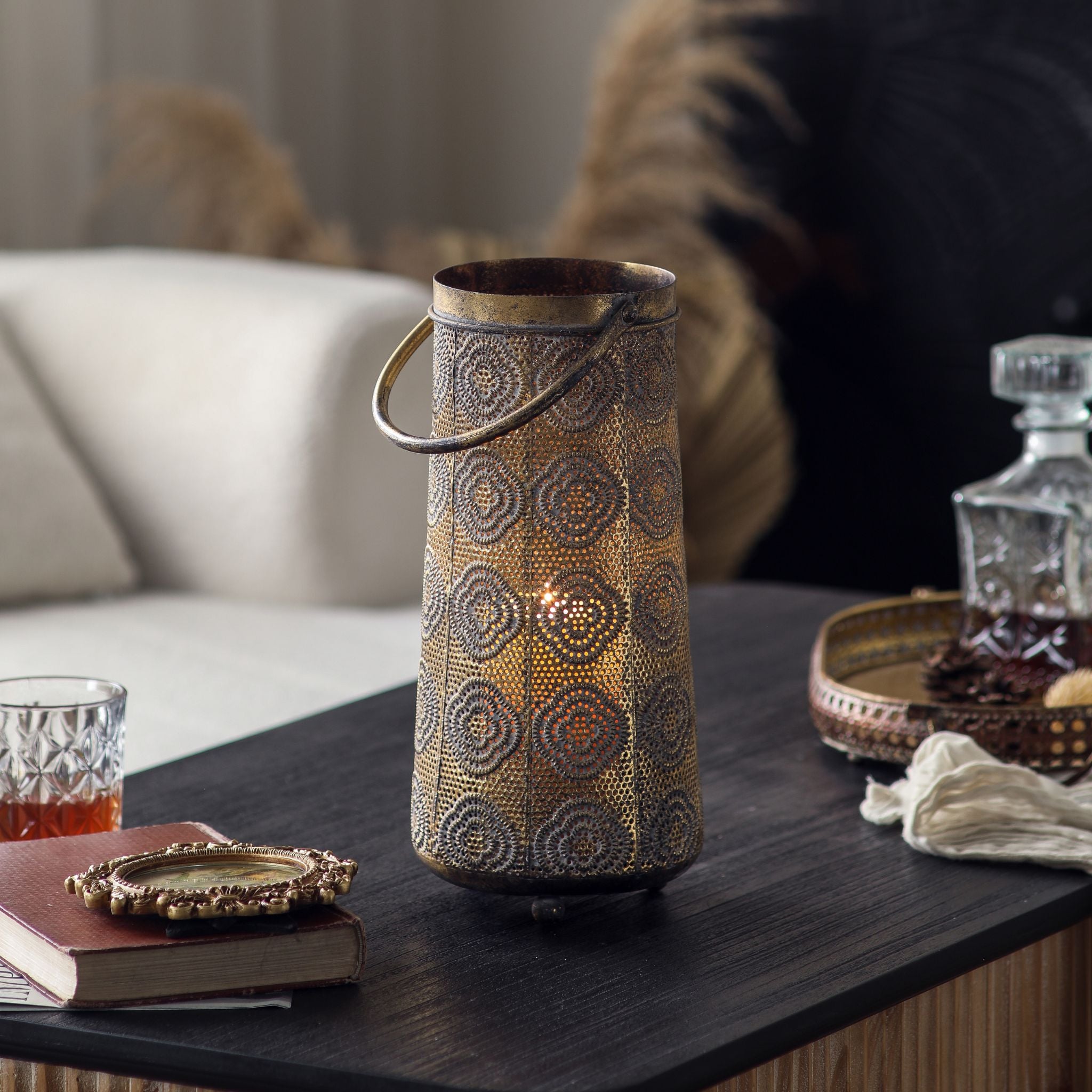 Jasmine candle lantern lit in a living room setting beside a decanter, casting a warm glow