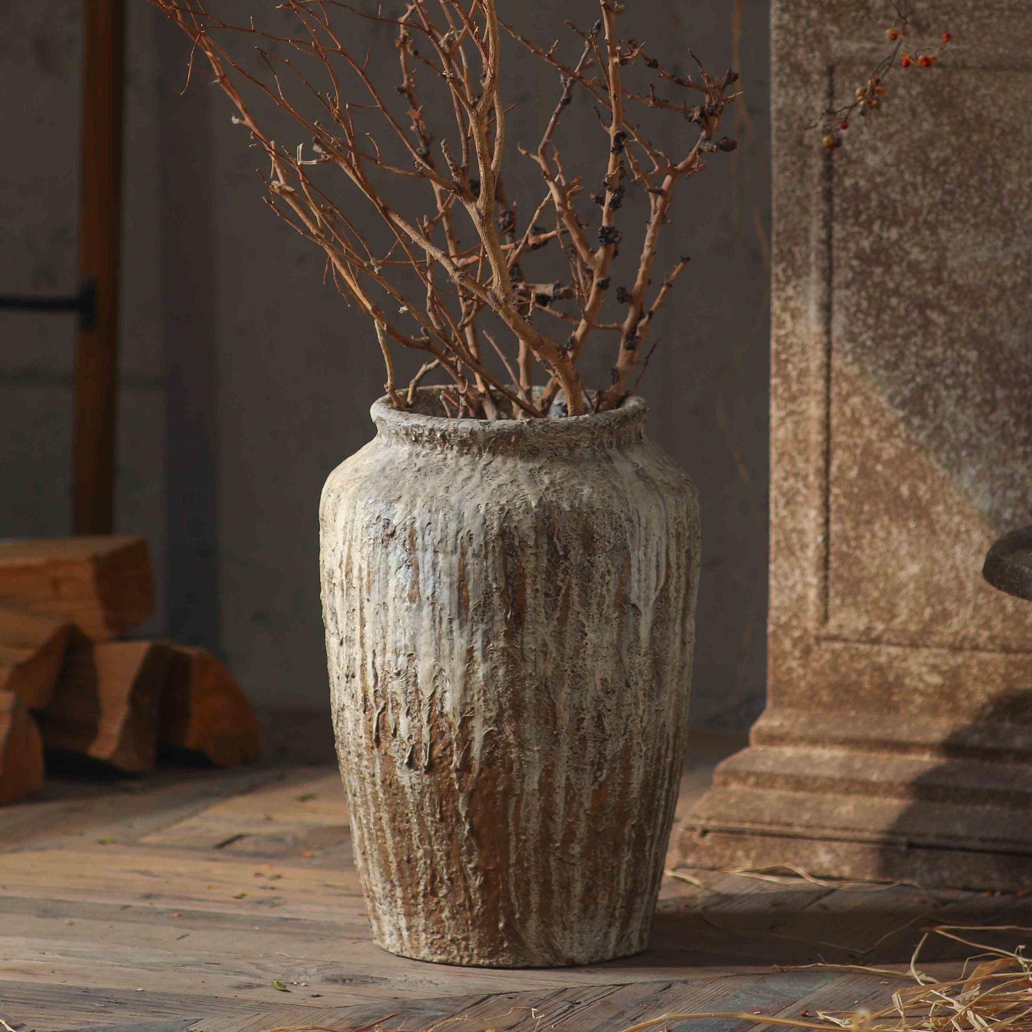 Jean-Marc tall jar vase on a timber floor against a stone column, styled with bare branches.