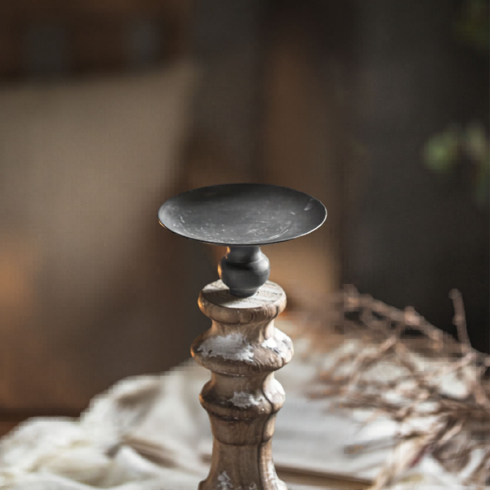 Close-up of the dark aged-metal dish and turned timber column top of the Jean candle holder.