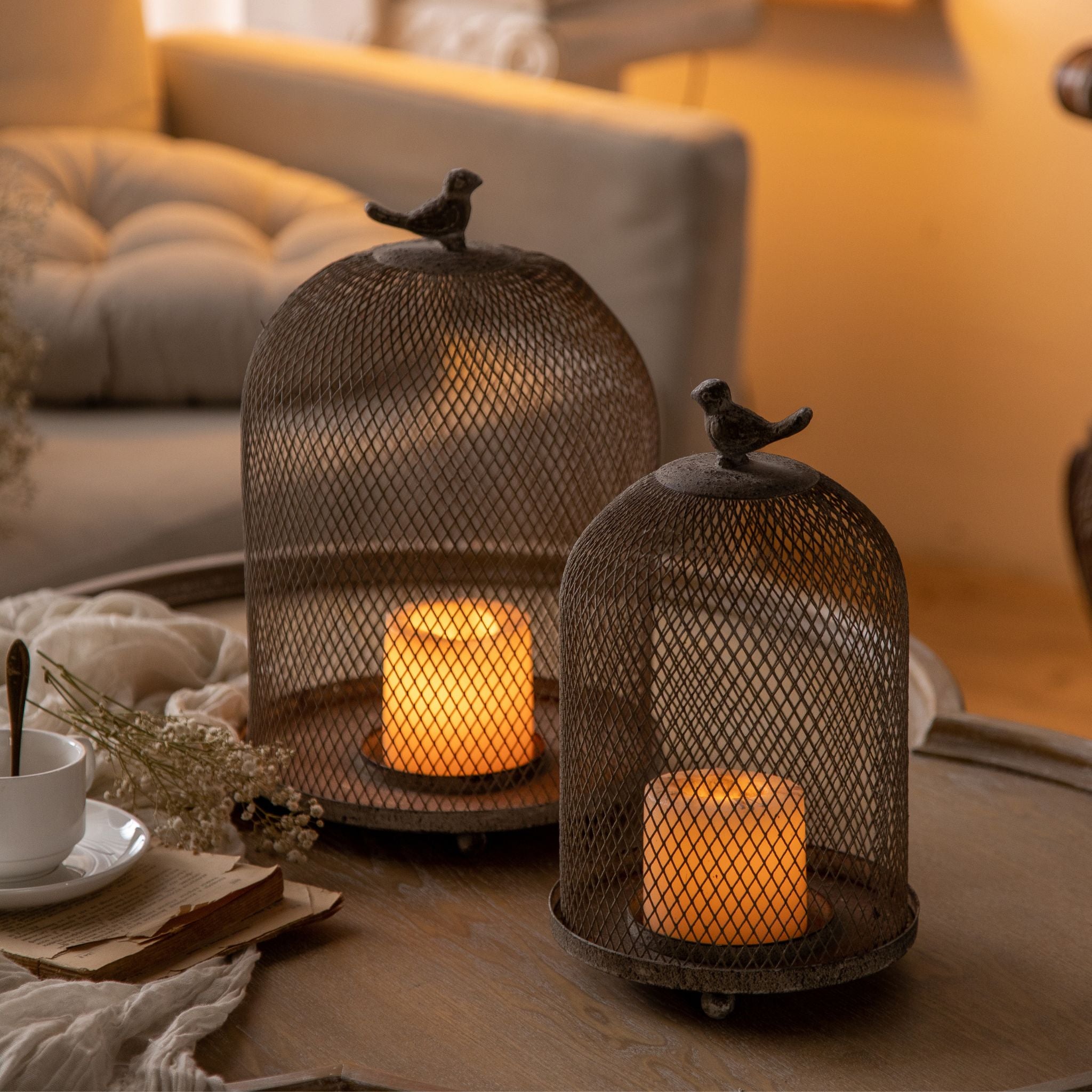 Joel set of two wire-mesh candle cloches with bird finials, lit, larger and smaller domes. Hero.