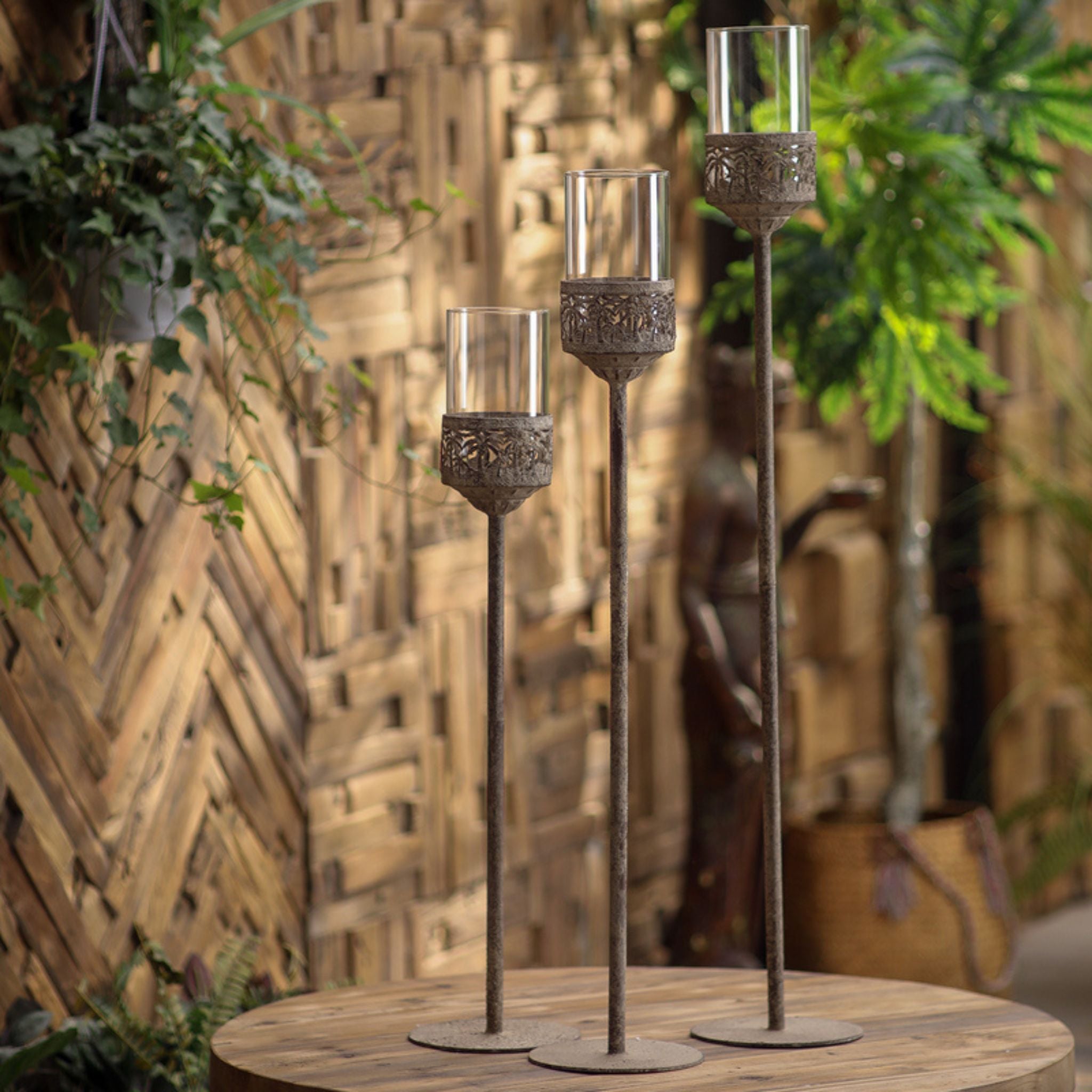 Three aged metal floor candle holders with glass hurricanes on a round timber table