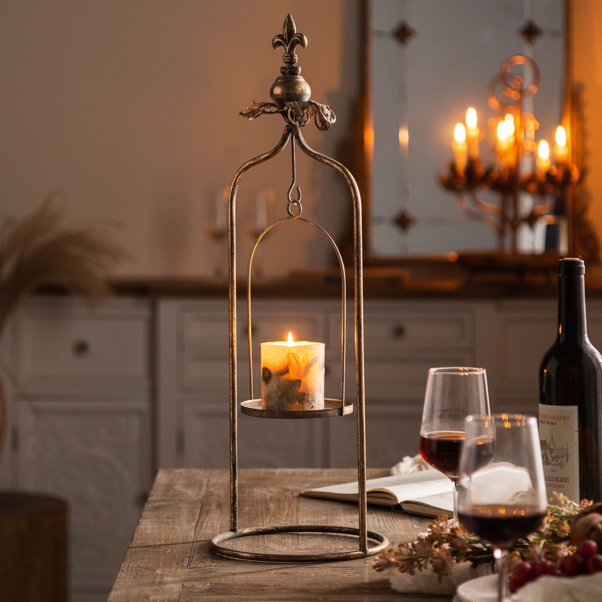 Julien candle holder with a lit pillar candle in the cradle, styled on a sideboard with a mirror and candle sconce behind.