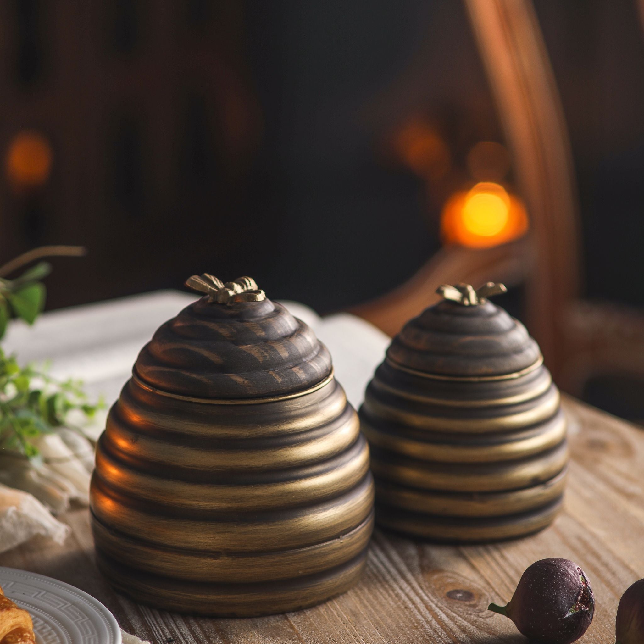 Leonie beehive honey pot set of two in antique gold metal with turned timber lids and brass bee finials, larger and smaller pots side by side. Hero.