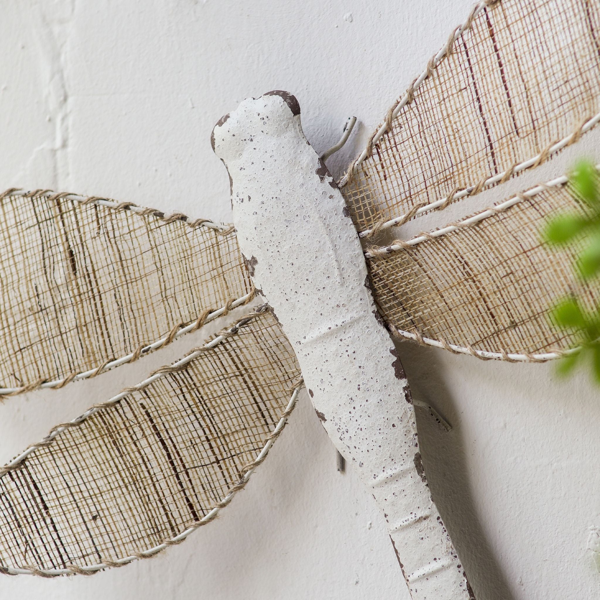 Close view of the chipped white metal body and the hemp rope edging where the jute wings meet the dragonfly