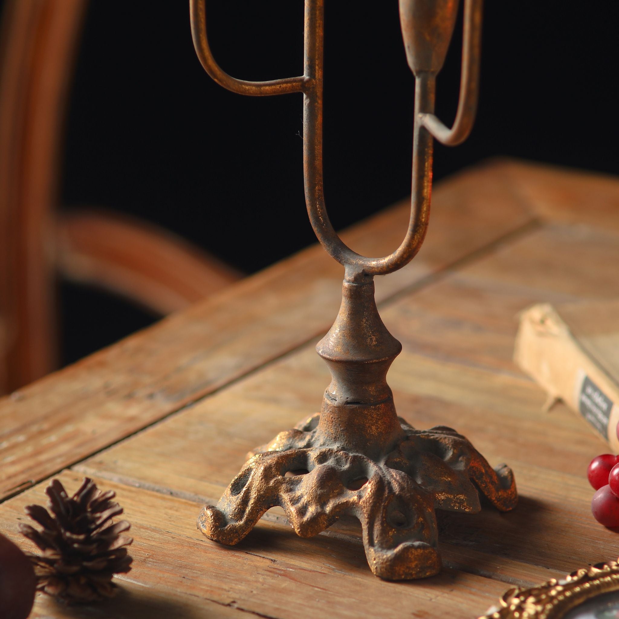 Close detail of the Lisette candelabra base, an ornate scrolled antique gold footed base on a timber table.