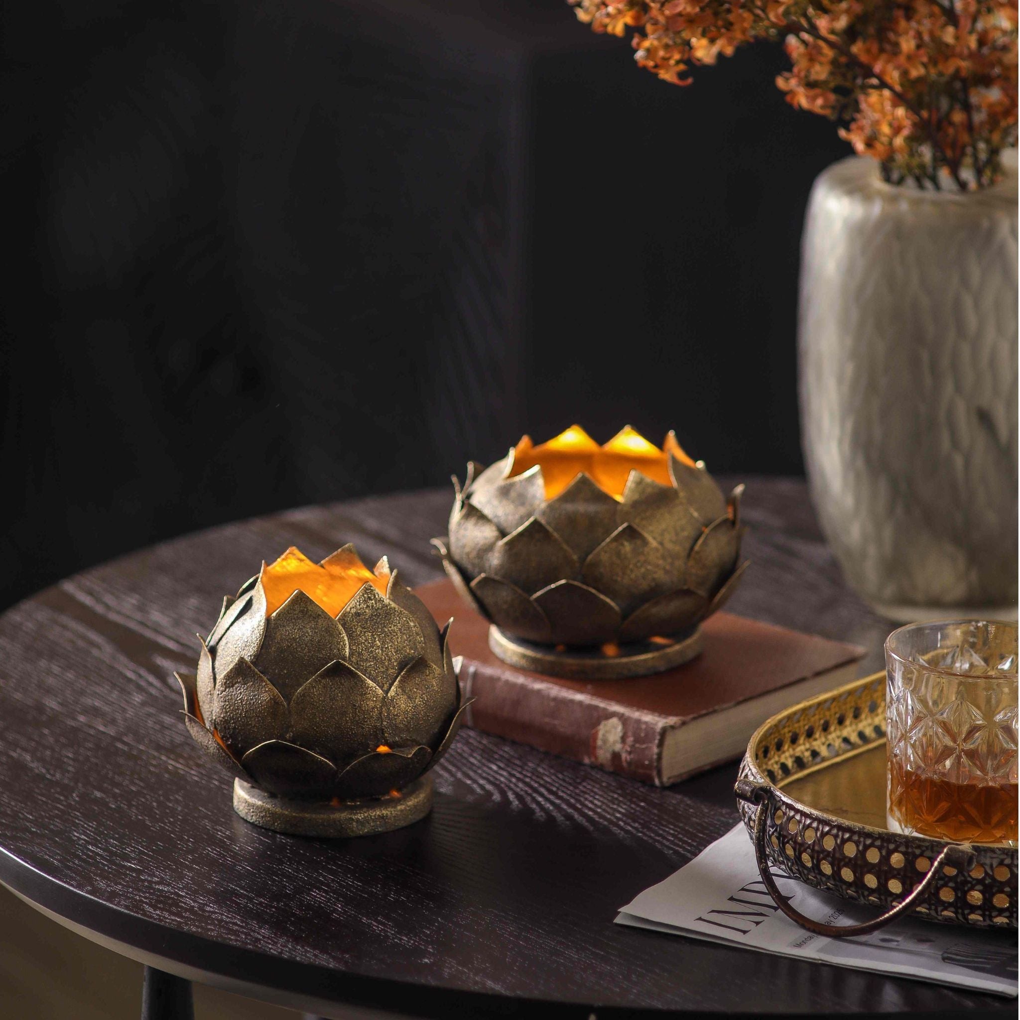 Victor set of two antique gold lotus tealight holders lit on a dark table with autumn branches. 