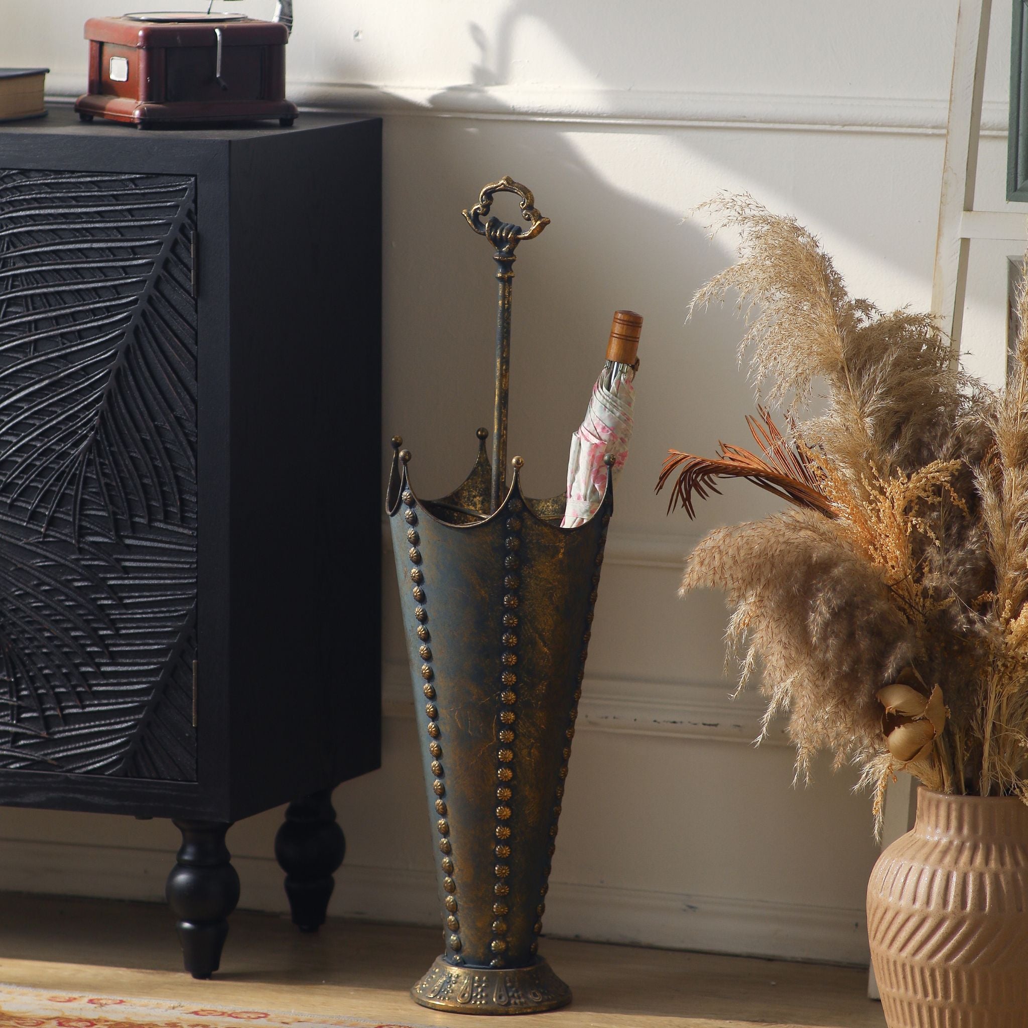 Luna French Provincial umbrella stand in antique gold metal with a crown-shaped top, standing in an entryway. Hero.
