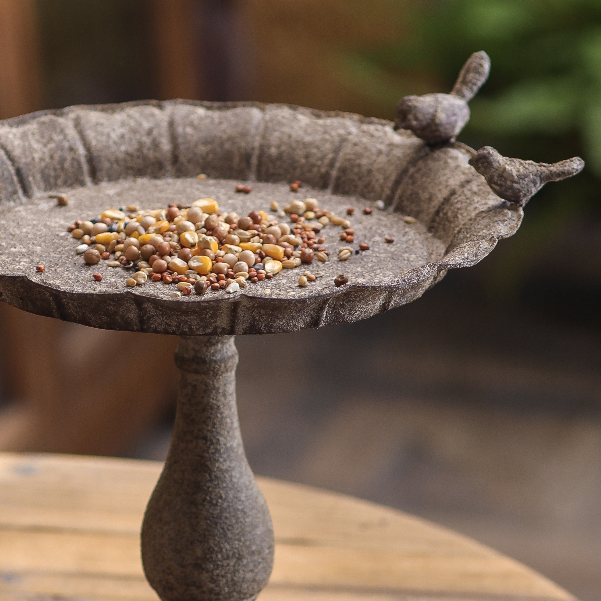 Manon iron pedestal bird feeder with seed in a French country garden setting