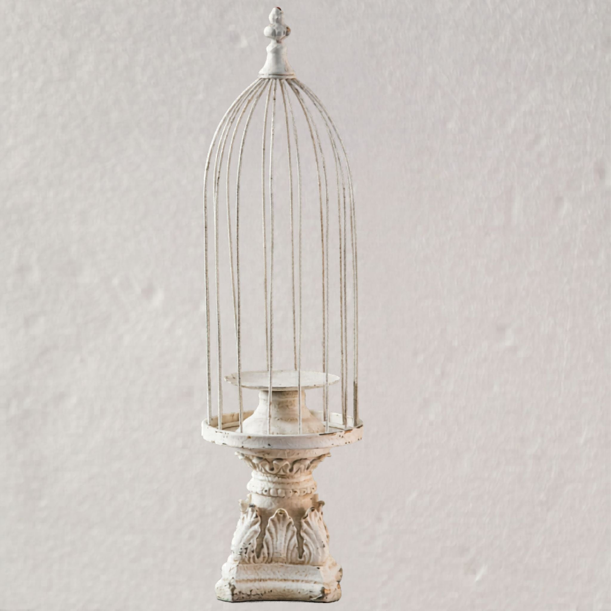 Matheo distressed-white birdcage candle holder shown empty, full domed cage with fleur-de-lis finial on an acanthus pedestal base.