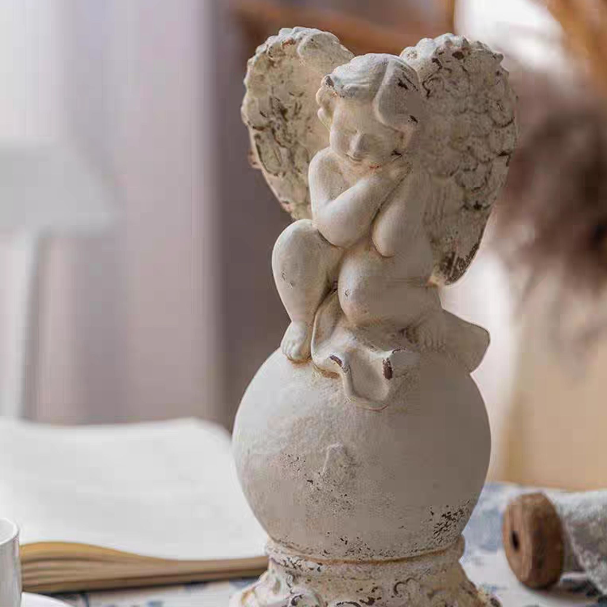 Close-up of Mathilde cherub finial showing the dozing pose, folded wings, and chipped whitewash on the orb
