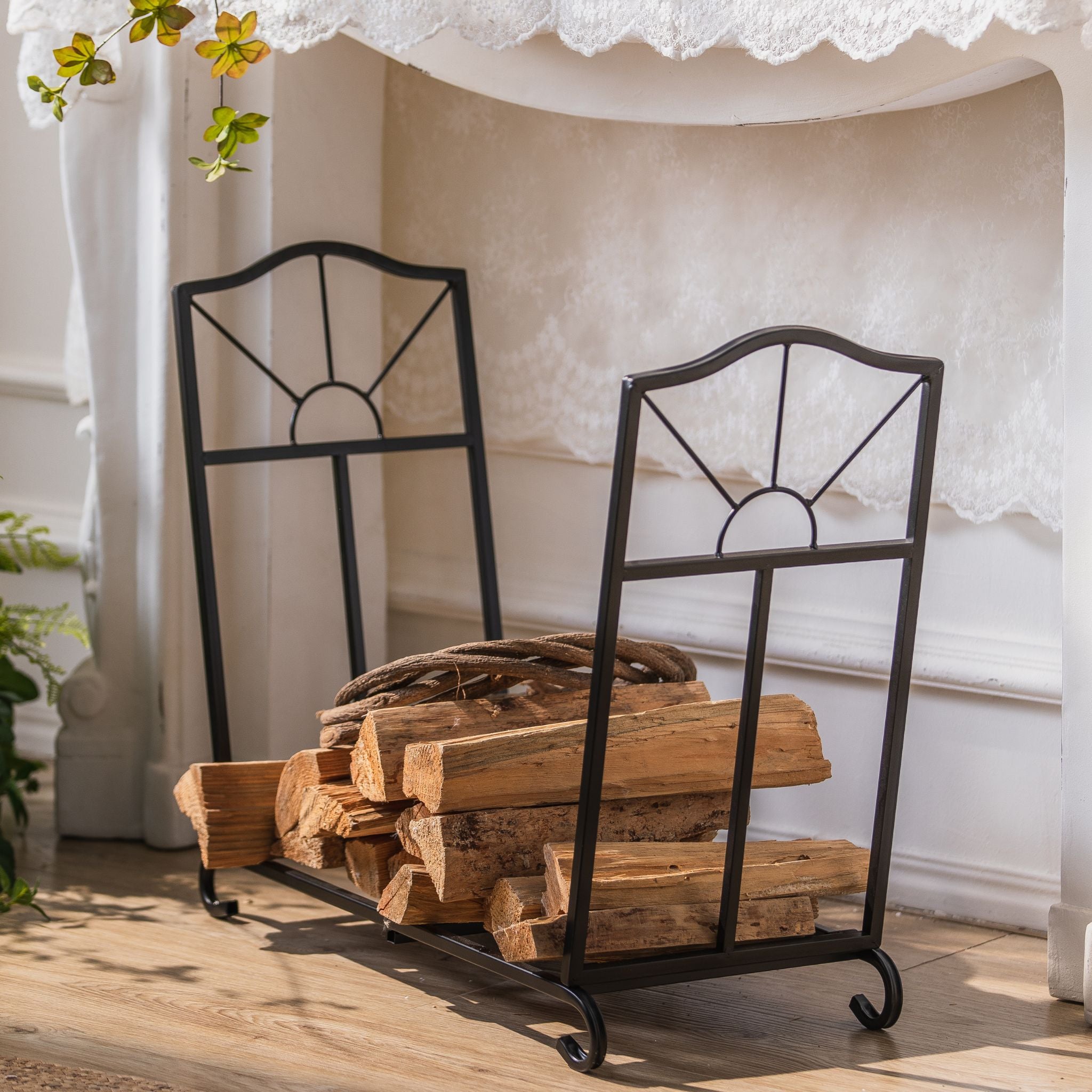 Adrien low matte black firewood log holder with sunburst fan sides, loaded with split logs by a fireplace. Angled view