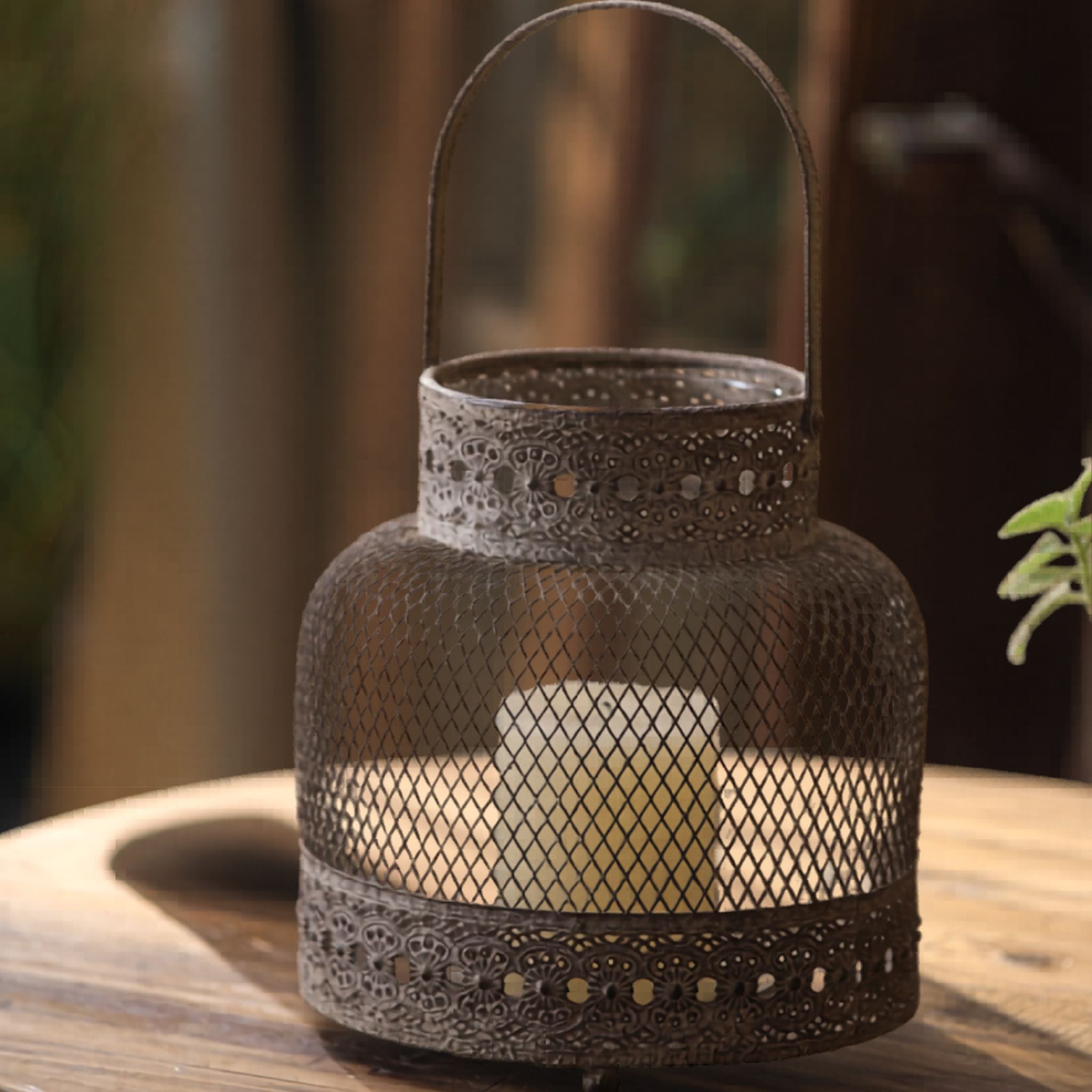 Small mesh candle lantern with arched handle glowing on a wooden table