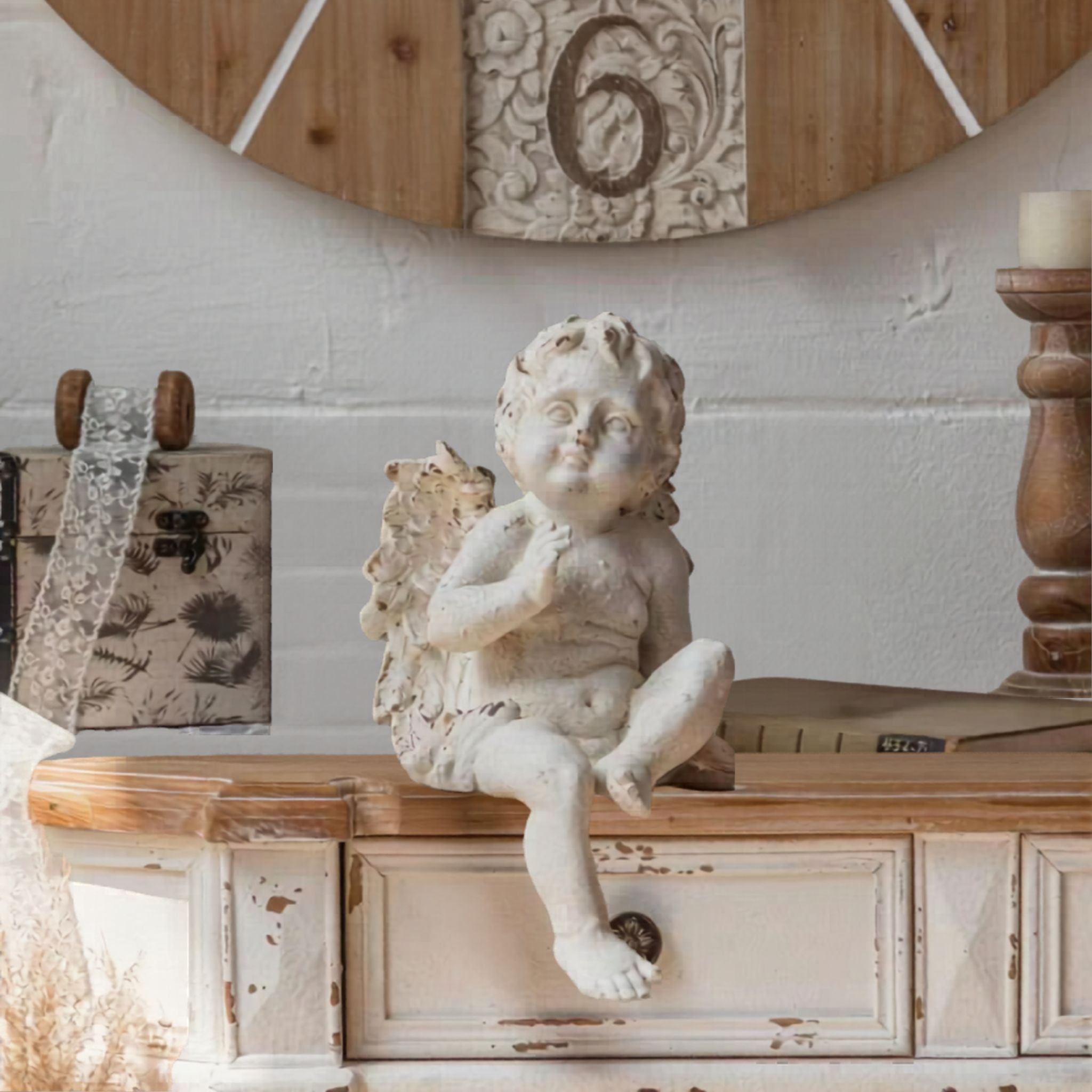 Maxime French Provincial cherub figurine in distressed whitewash, seated on a wooden console with one leg dangling, styled with a tall candle and architectural detail. Hero