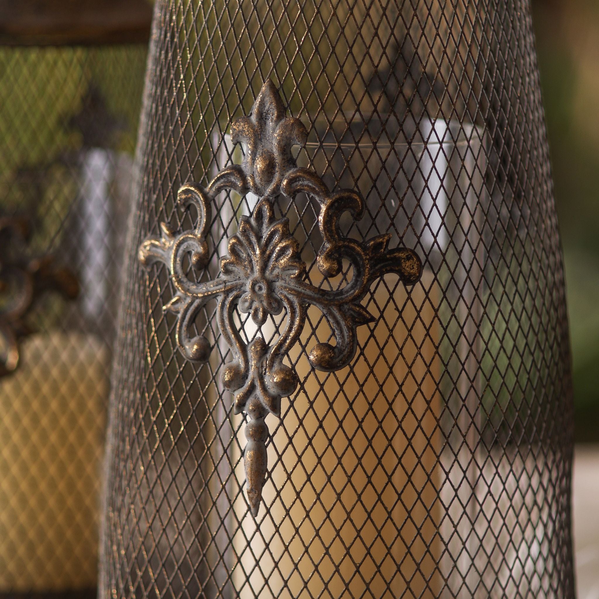 Close-up of Sophie candle lantern fleur-de-lis medallion over the clear glass insert with warm candle glow
