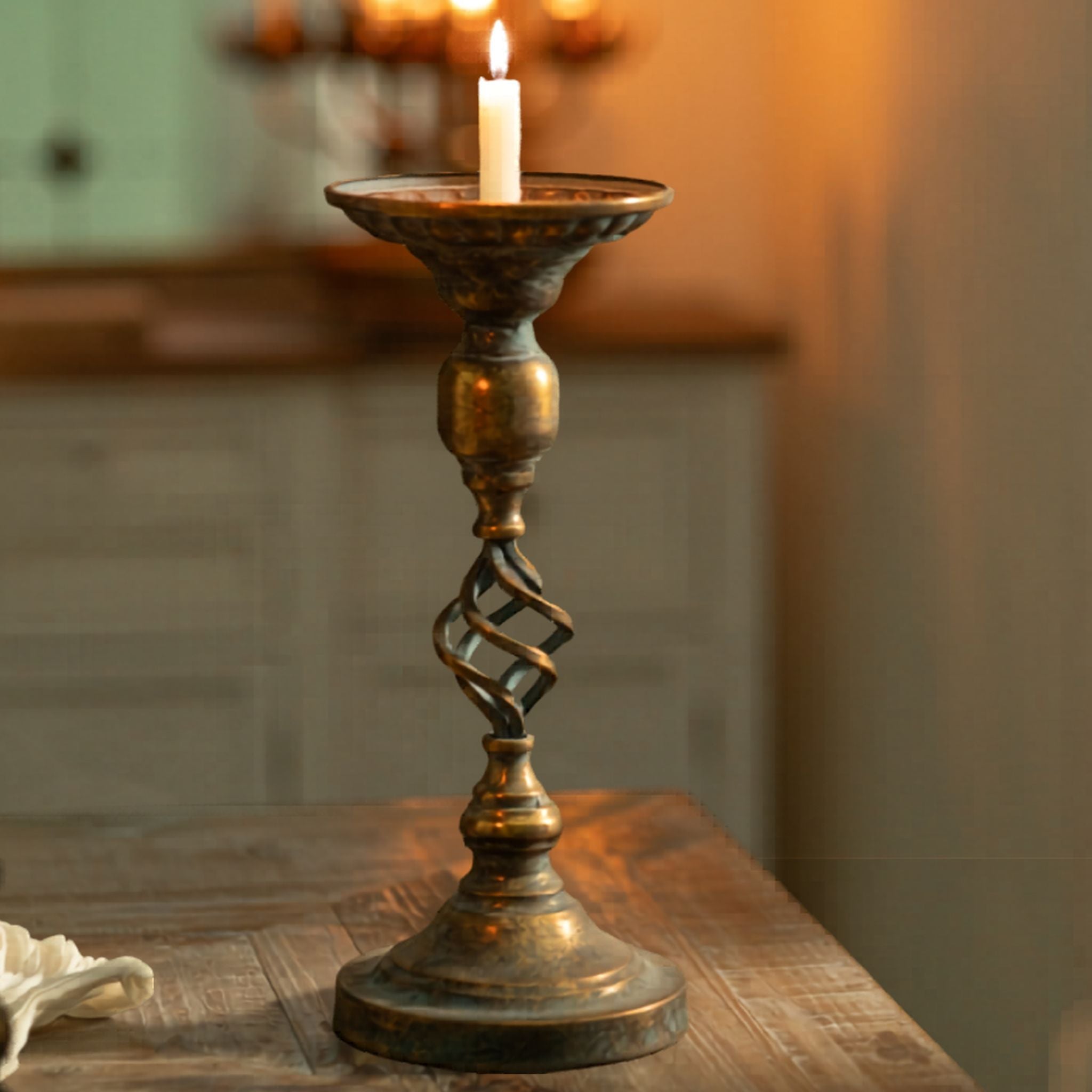 Michel French Provincial candle holder in antique gold and verdigris, twisted open-cage stem and turned ball knop, lit taper on a wood table. 
