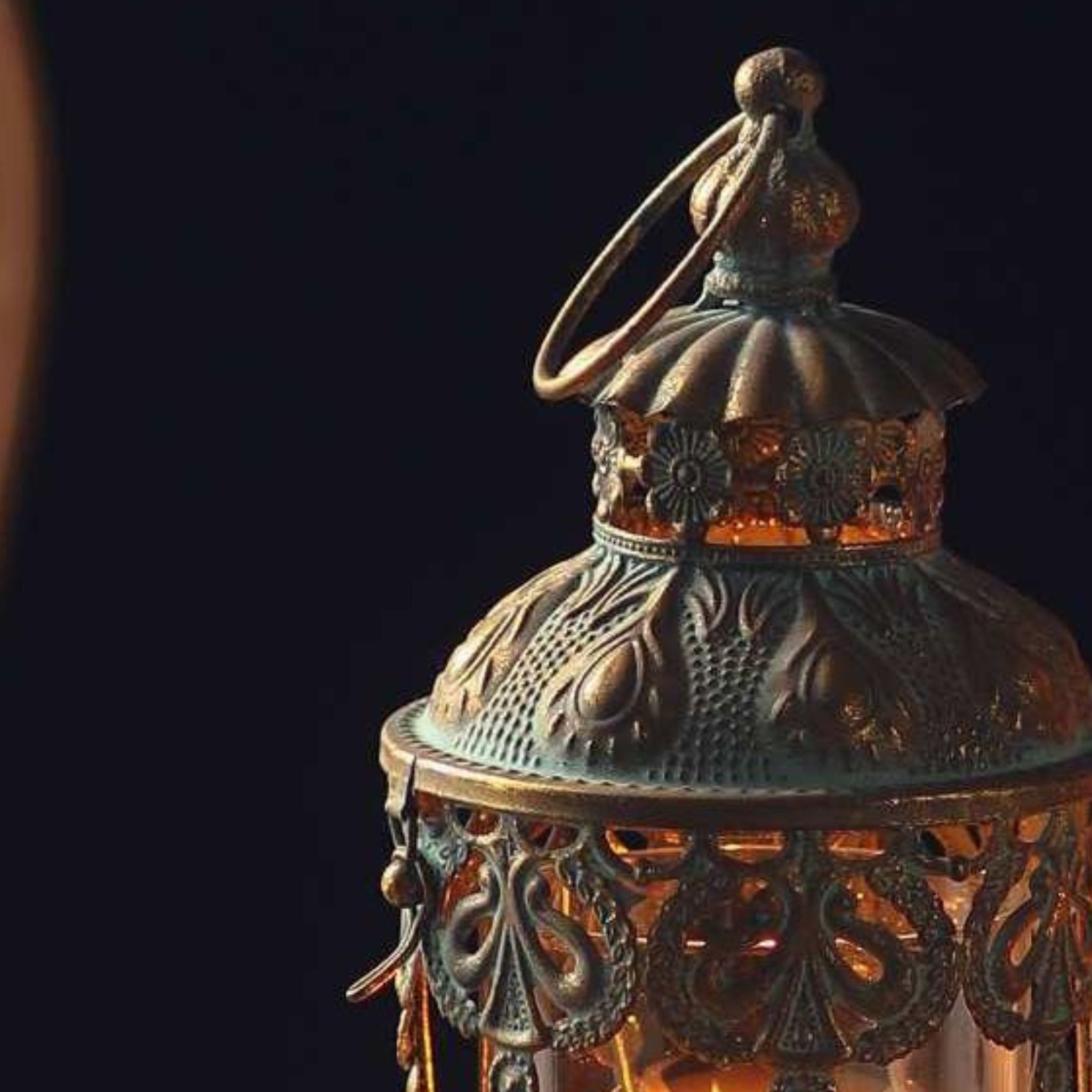 Mylan lantern dome lit from within, amber glow through the pierced filigree and embossed antique gold.