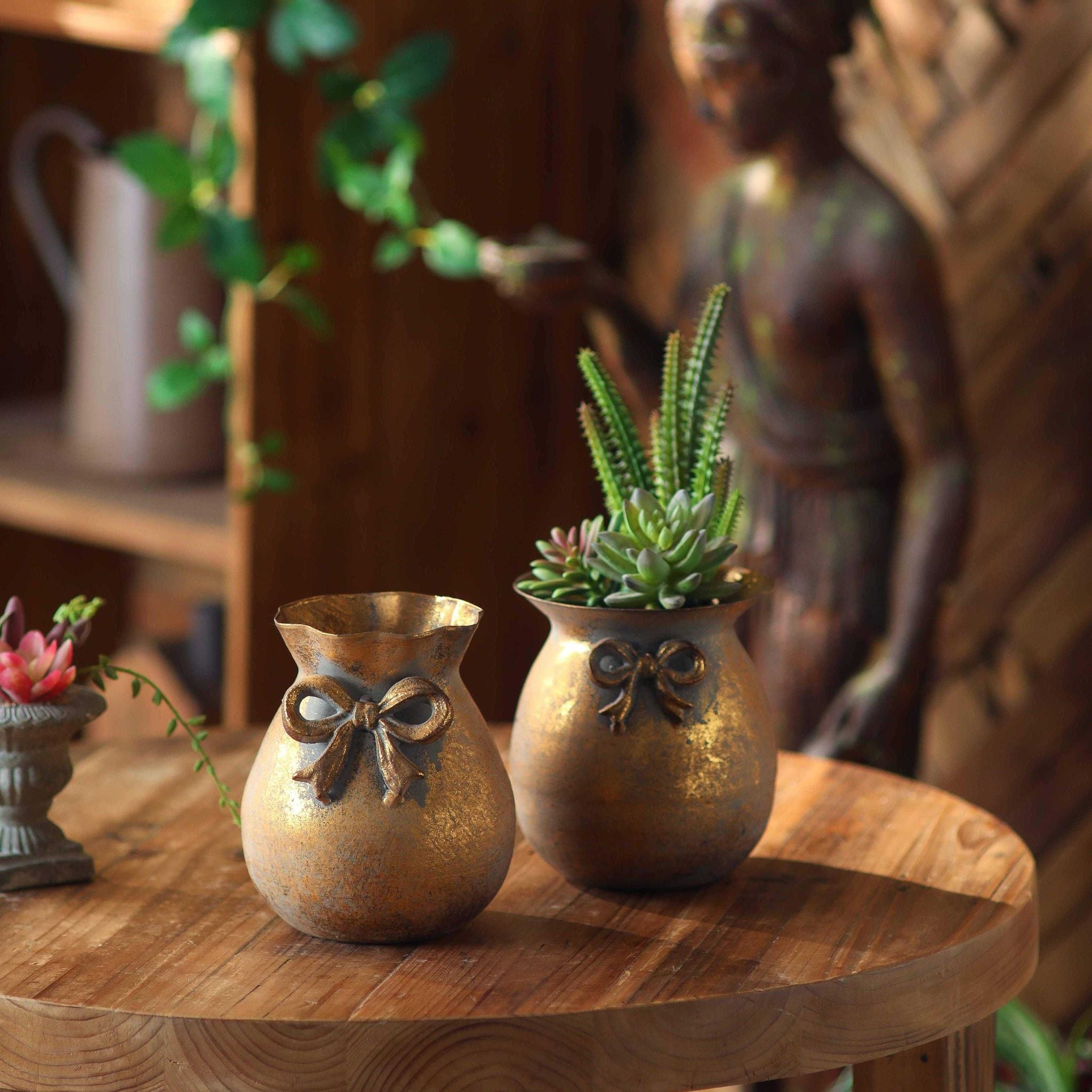 Noel pair of antique-gold bow pots styled on a round table, one planted.