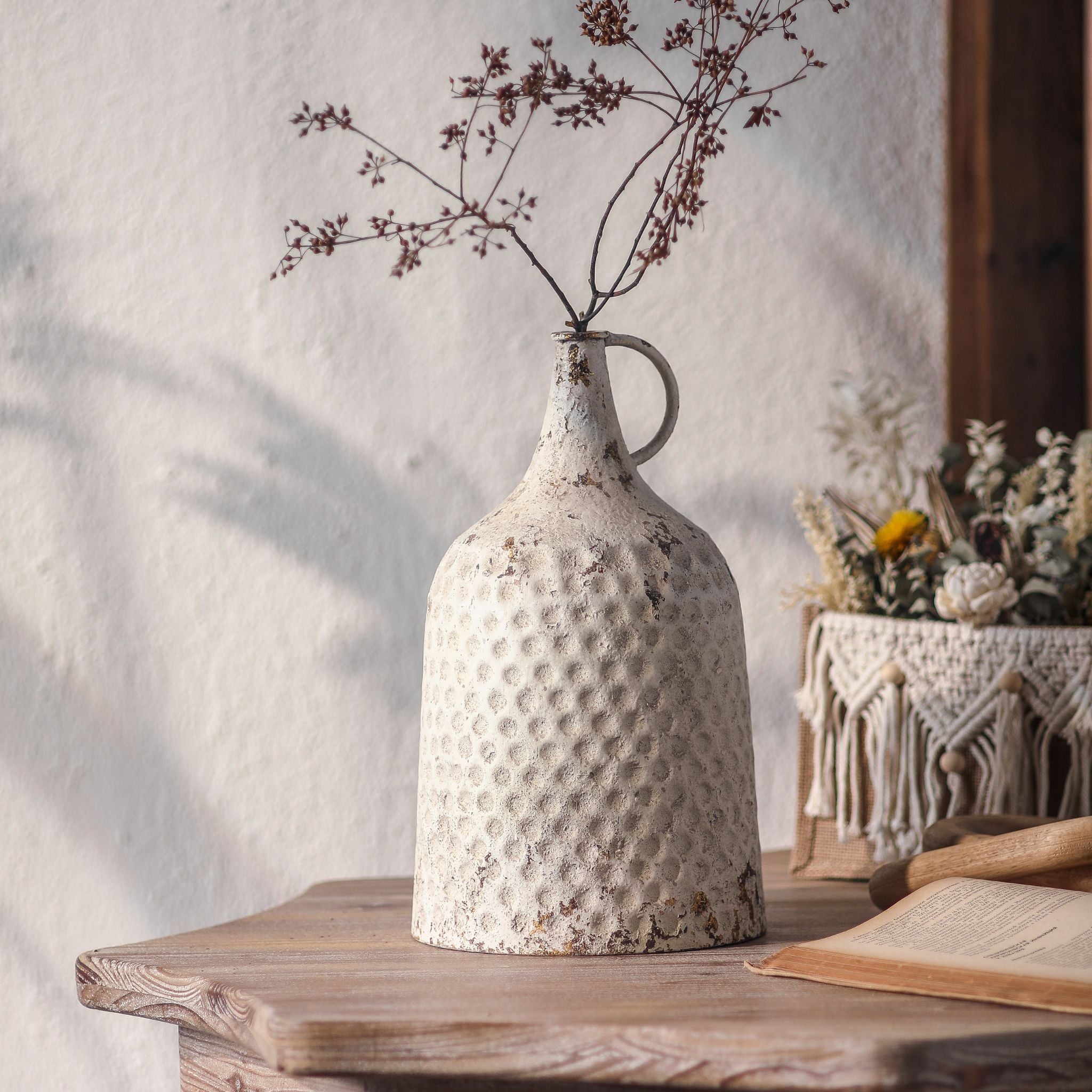 Noemie hammered-metal jug vase in distressed white with a loop handle, styled with dried branches. Hero