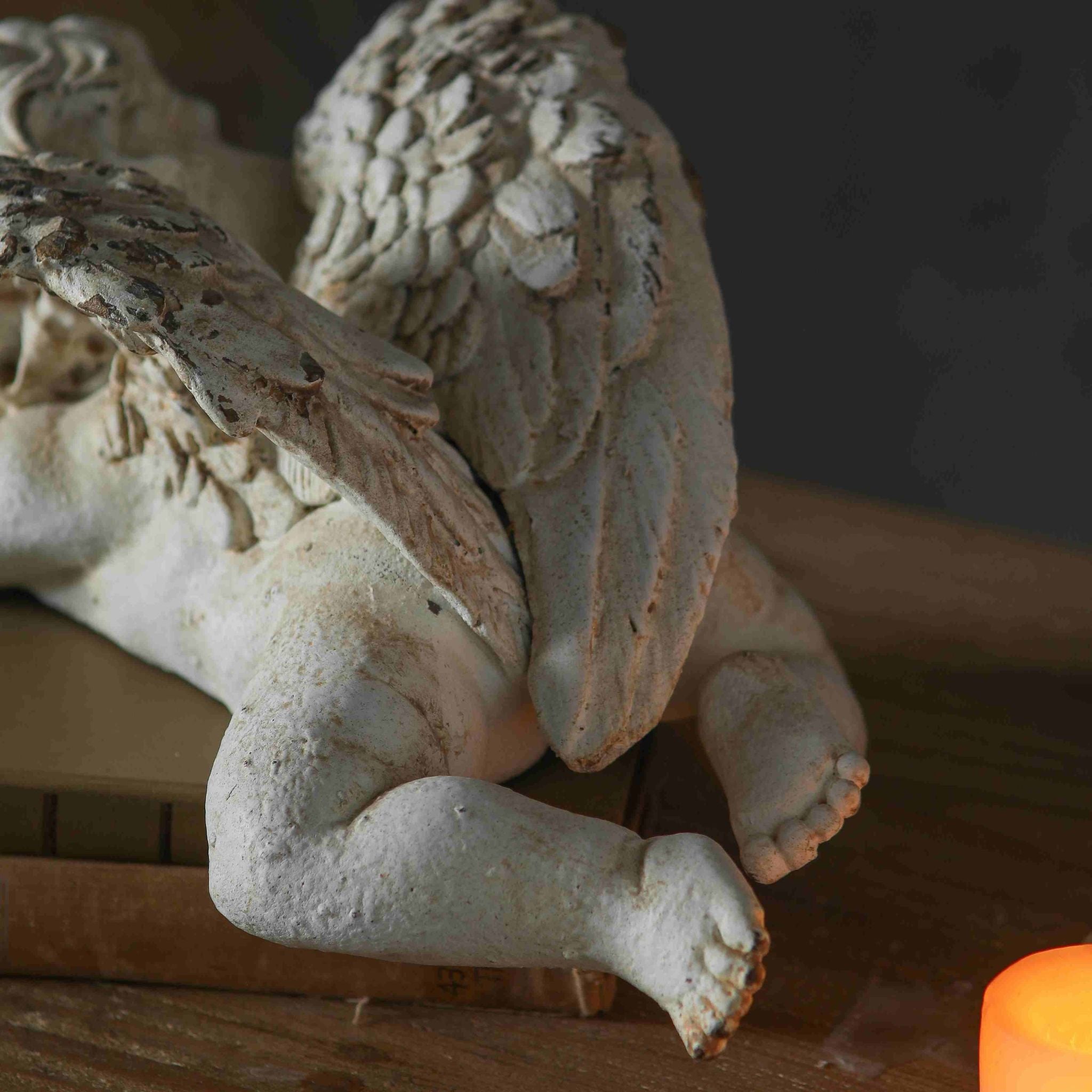 Close-up of Océane sleeping cherub wing and foot detail showing the deeply textured feathers and chipped whitewash revealing warm terracotta undertone