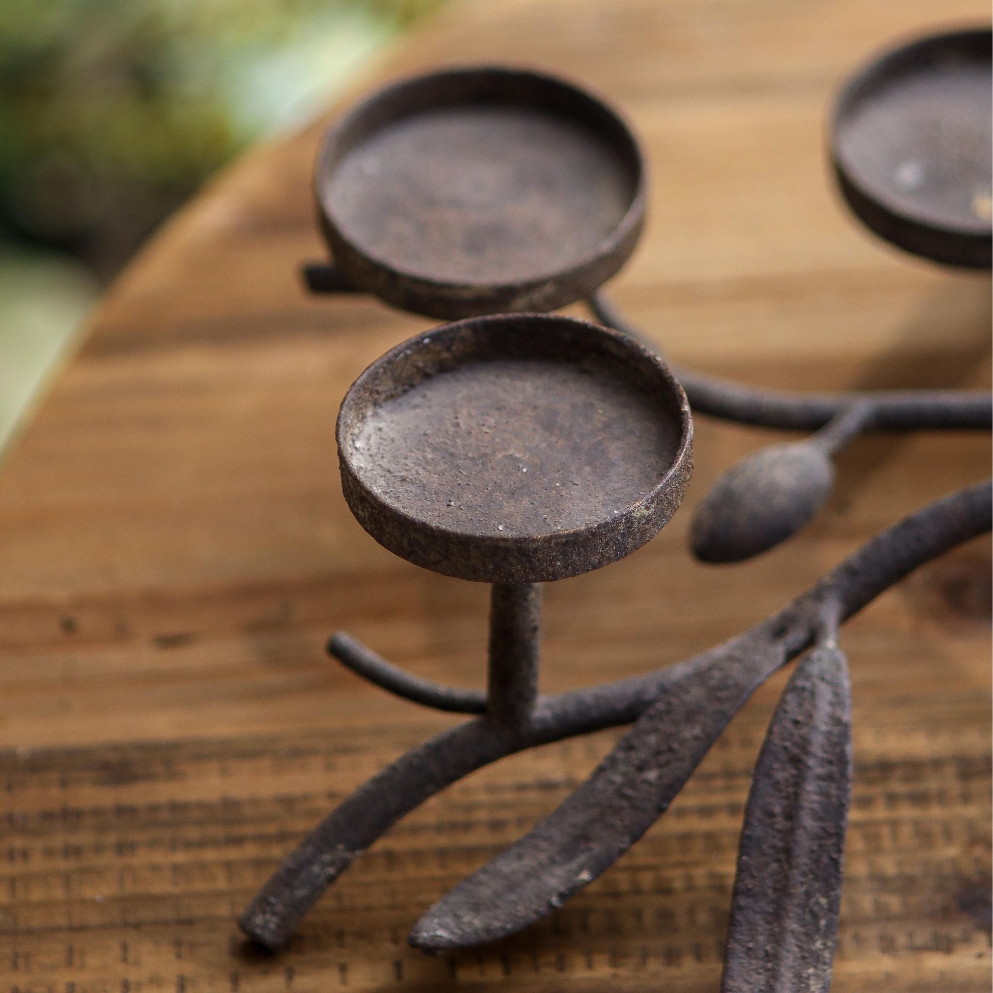 Close detail of the olive branch with cast olives and leaves and a candle plate in dark aged metal.