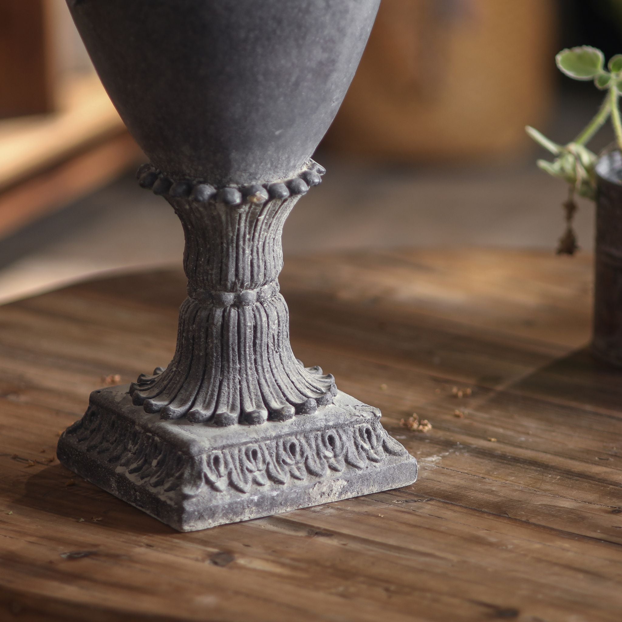 Close-up of the Patrick urn reeded stem and leaf-tipped square plinth in dark lead-grey.