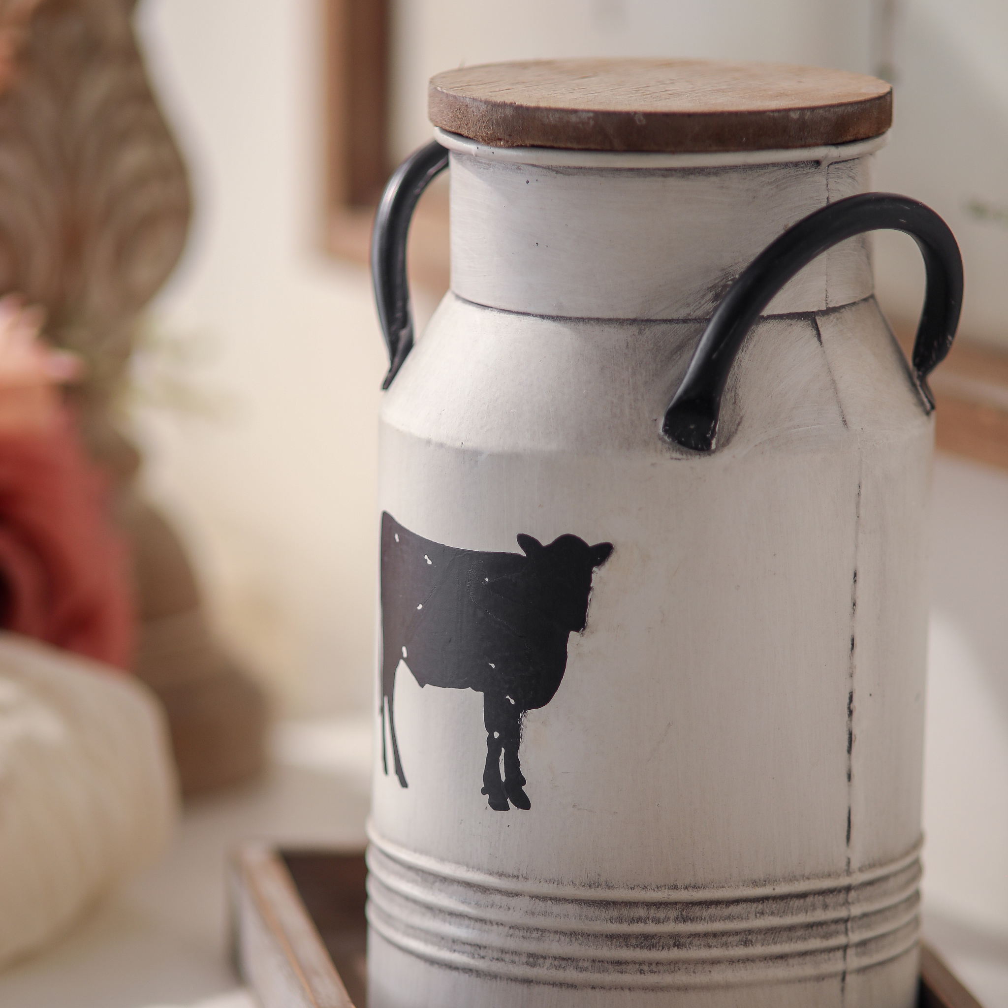 Close-up of single farmhouse milk can canister with cow silhouette showing distressed white finish wooden lid and black iron handles