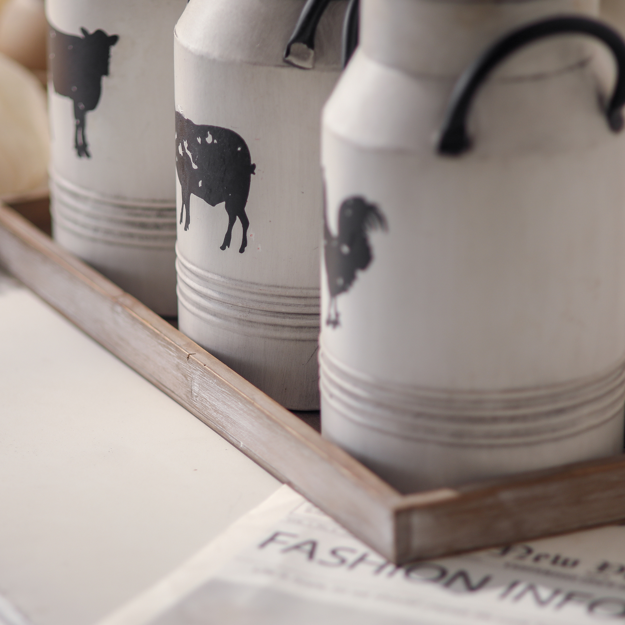 Side profile of three Petite Ferme milk can canisters showing ribbed banding and animal silhouettes on wooden tray