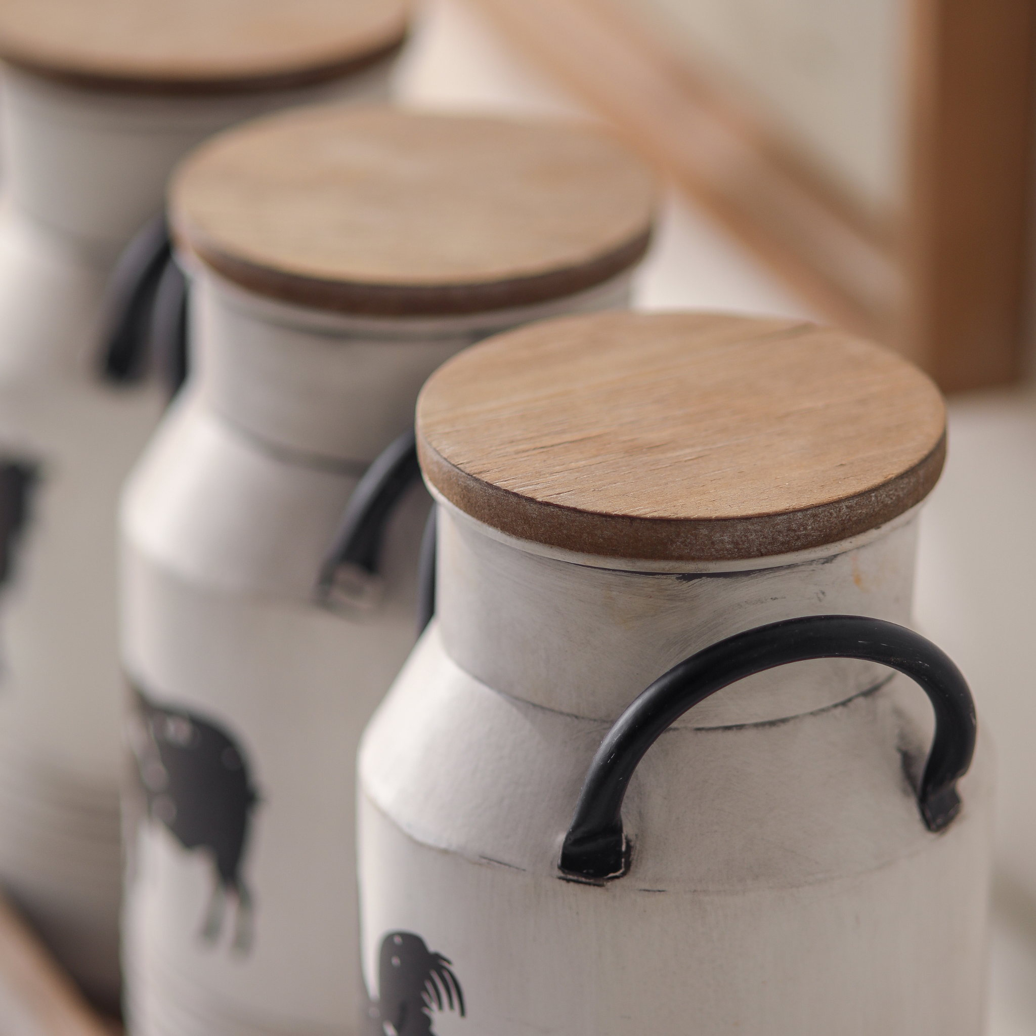 Close detail of wooden lids and curved black iron handles on Petite Ferme milk can canisters