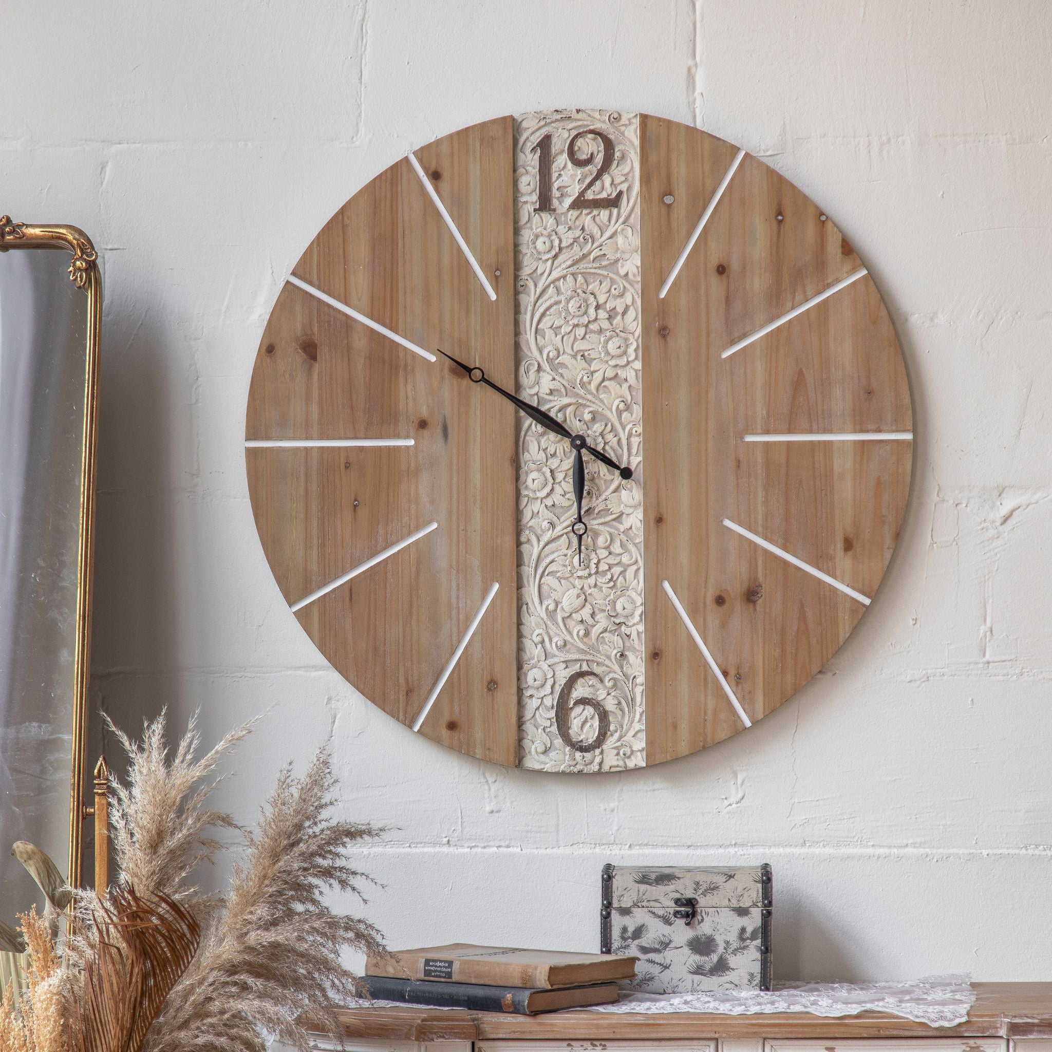 Pierre French Provincial wall clock with carved whitewashed floral panel on natural fir wood, mounted above a console with pampas grass, gilt mirror, and styled books. Hero