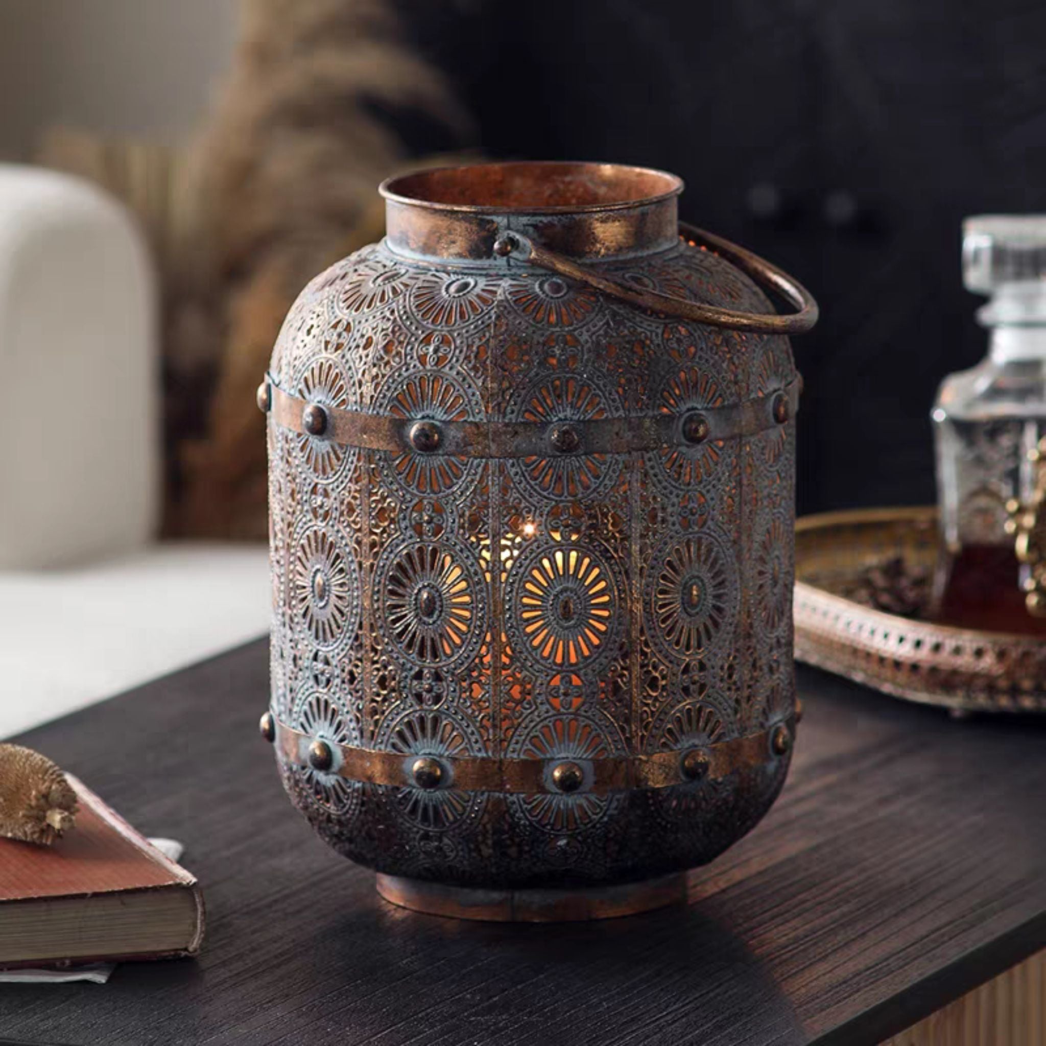 Rachelle Moroccan pierced metal candle lantern in antique copper and verdigris, lit, with a swing handle. Hero.