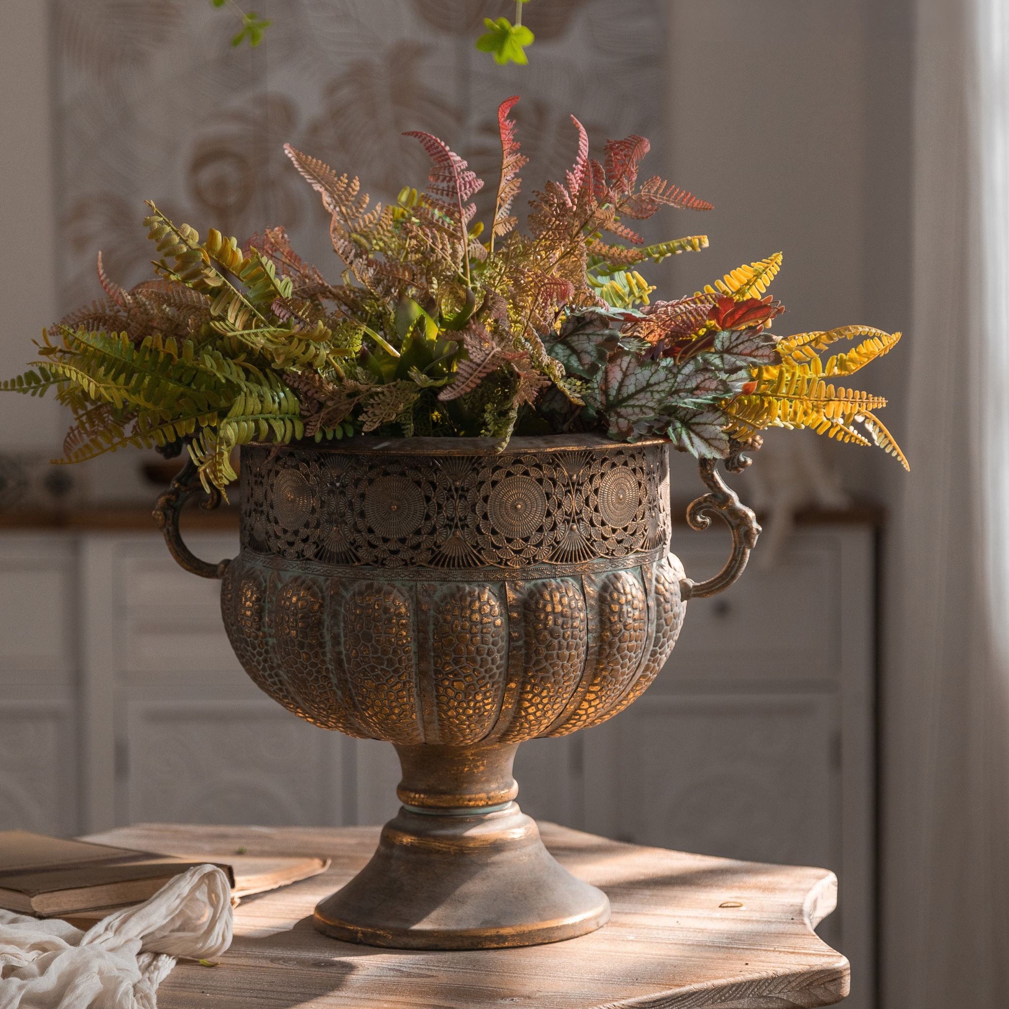 Regis aged metal footed urn planter filled with autumn ferns on a timber table. Hero