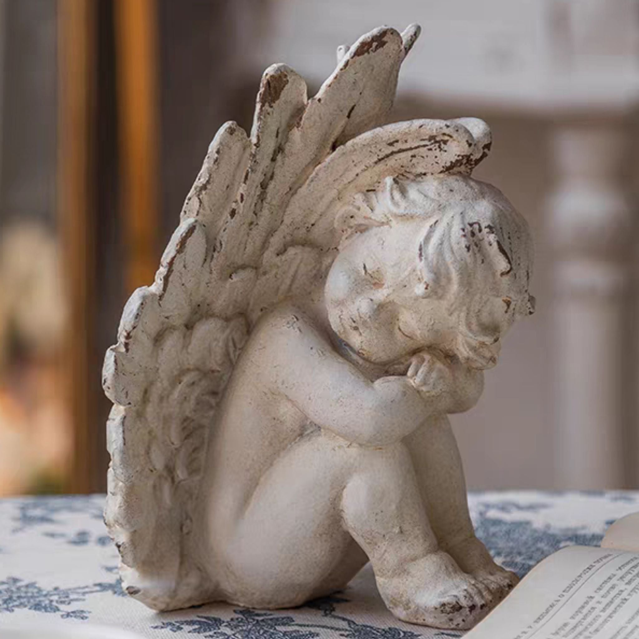 Romain cherub figurine styled alongside an open vintage book on a blue toile cloth, warm natural light