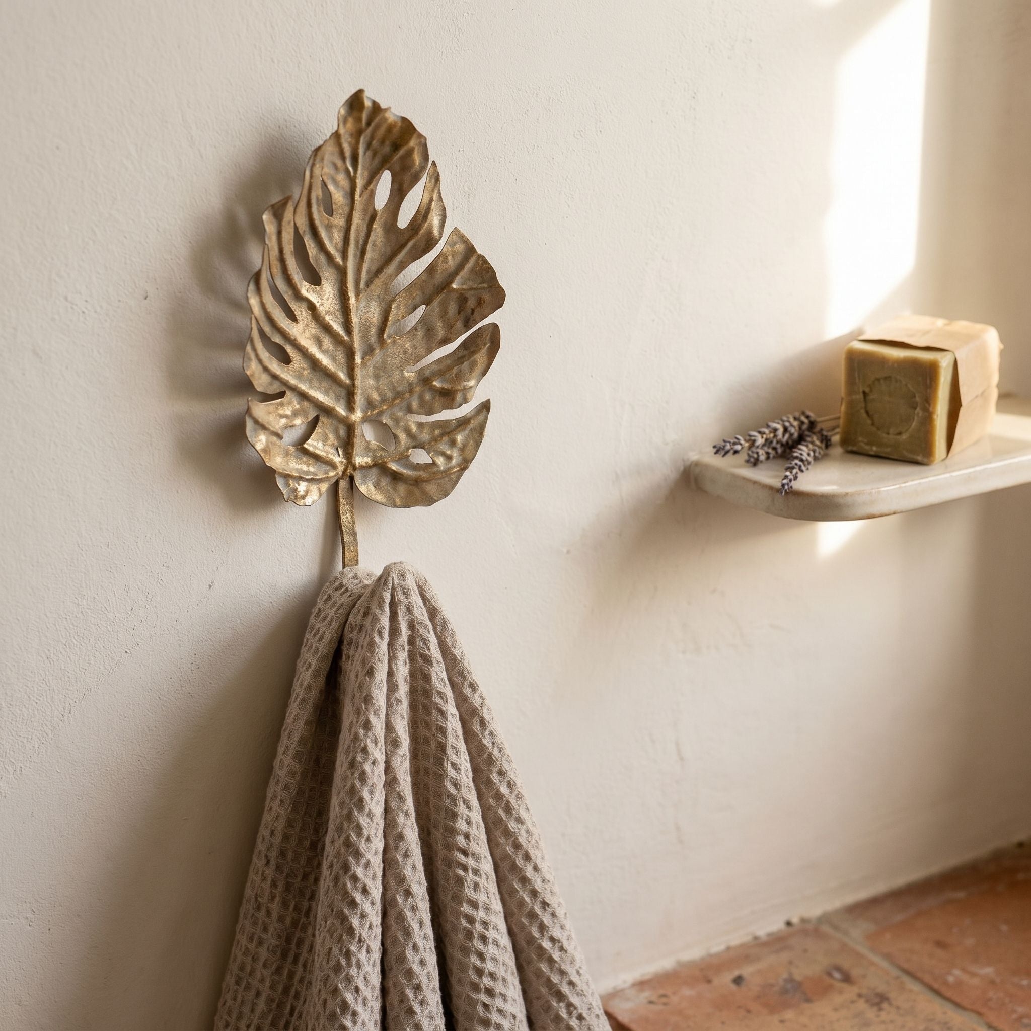 Roxane leaf wall hook close up, mottled antique gold aged metal with split-leaf fenestrations, holding a waffle towel.