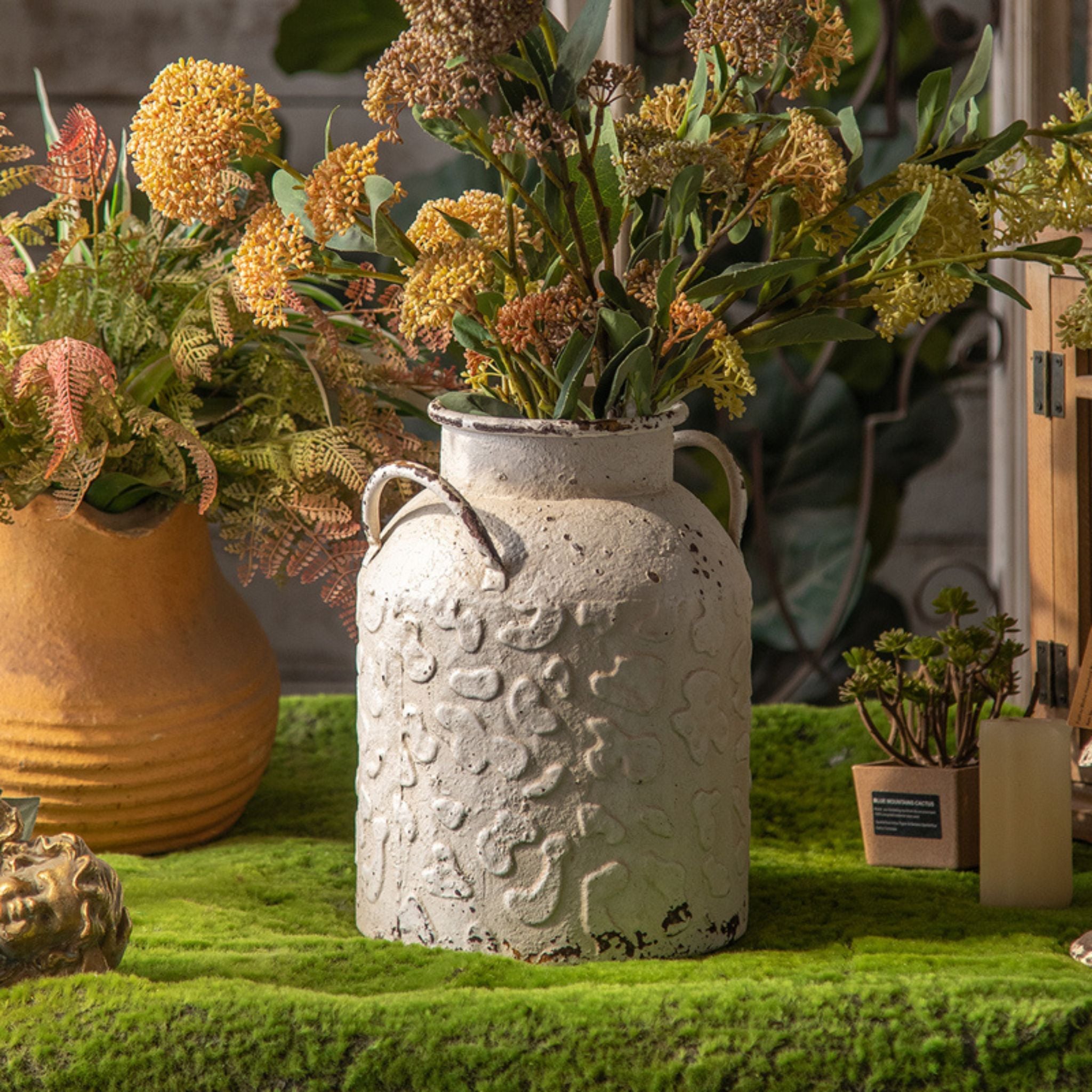 Serge milk churn vase filled with dried yellow and green stems, styled in a garden setting.