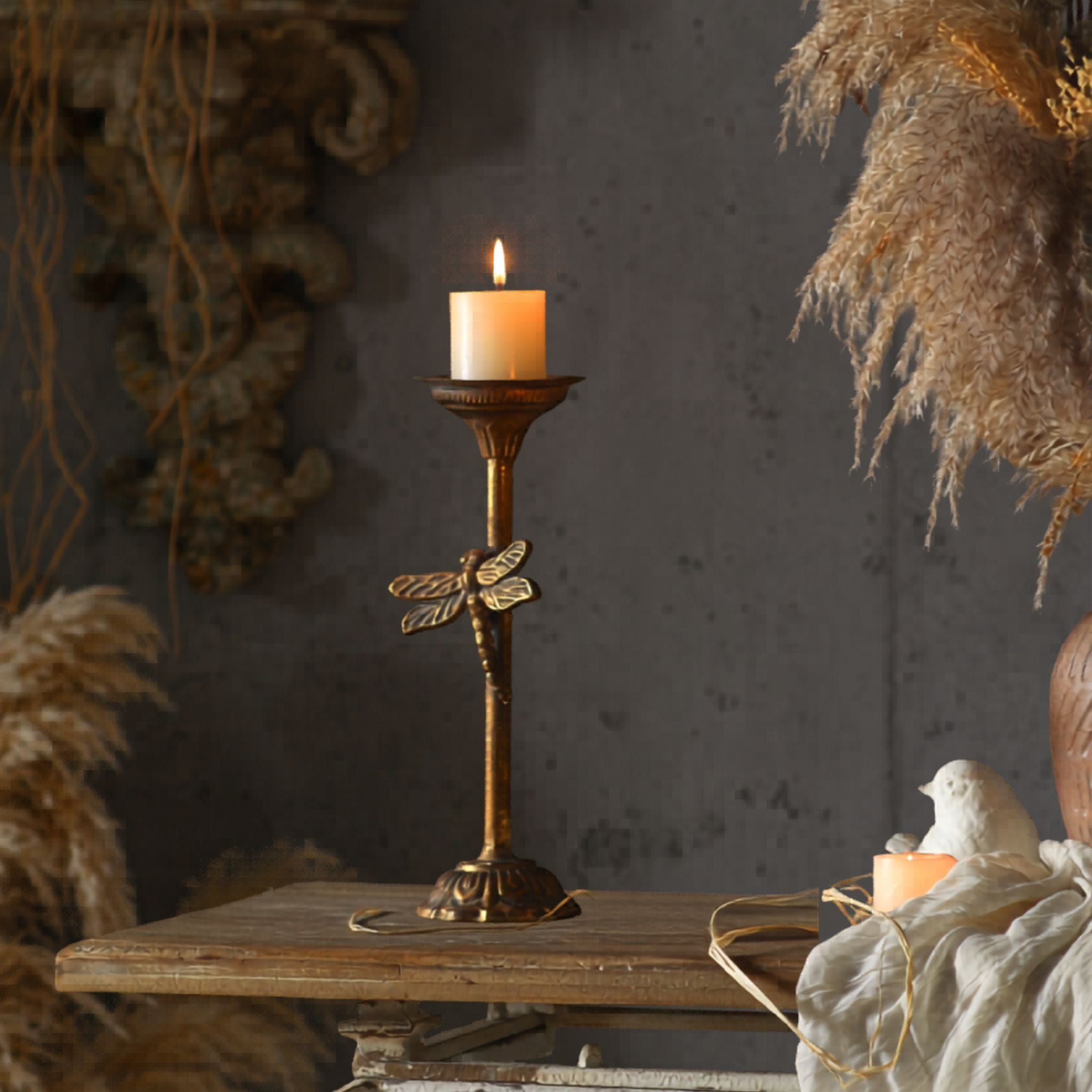 Lara dragonfly candlestick in aged gold metal holding a lit pillar candle in a styled French Provincial setting