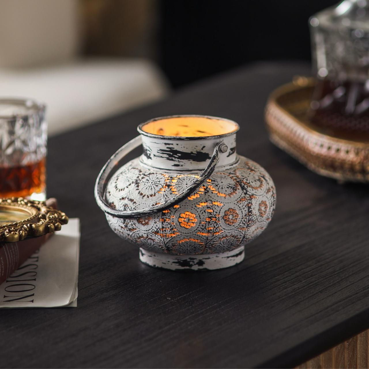 Soraya pierced aged metal tea light lantern lit on dark timber table, styled with whiskey decanter and gilt mirror