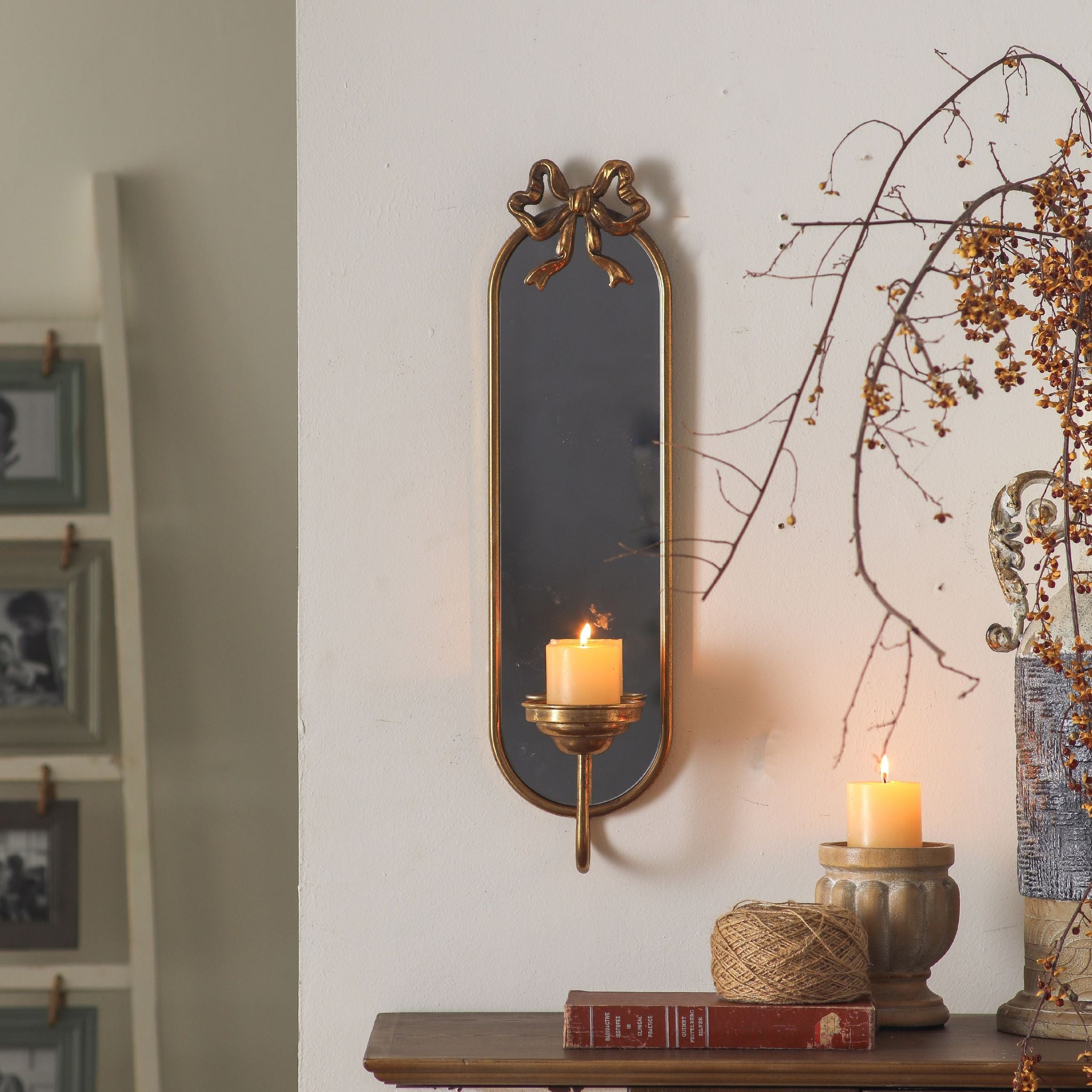 Aude mirror candle sconce styled above a console with books and dried stems